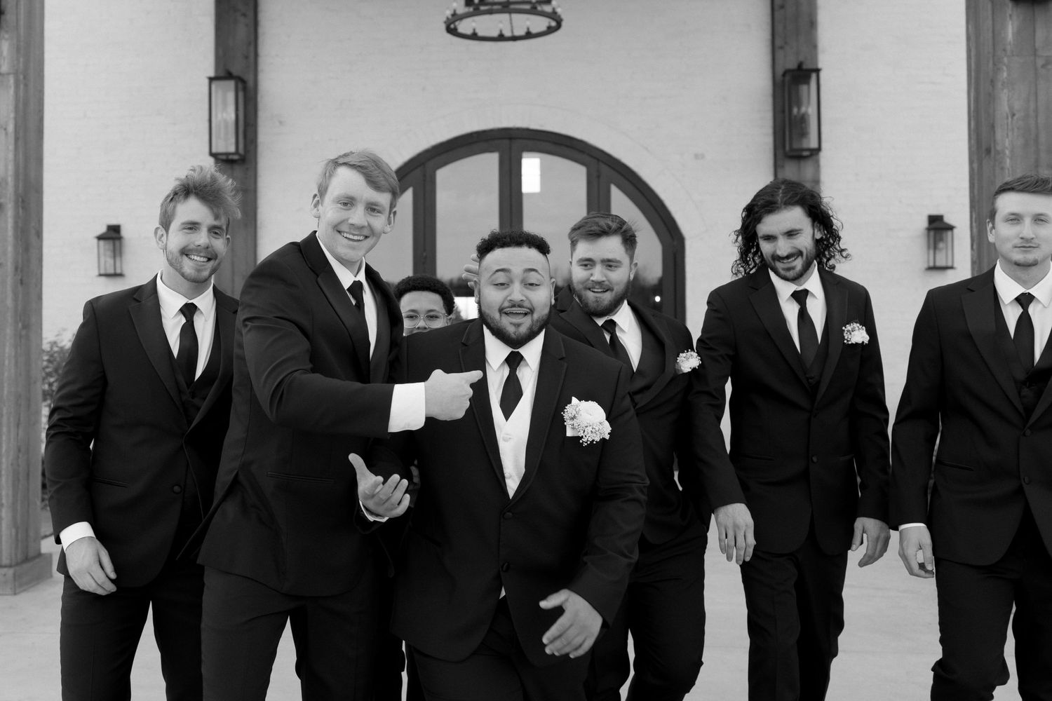 A groomsmen group shares a candid moment outside their wedding venue in black and white.