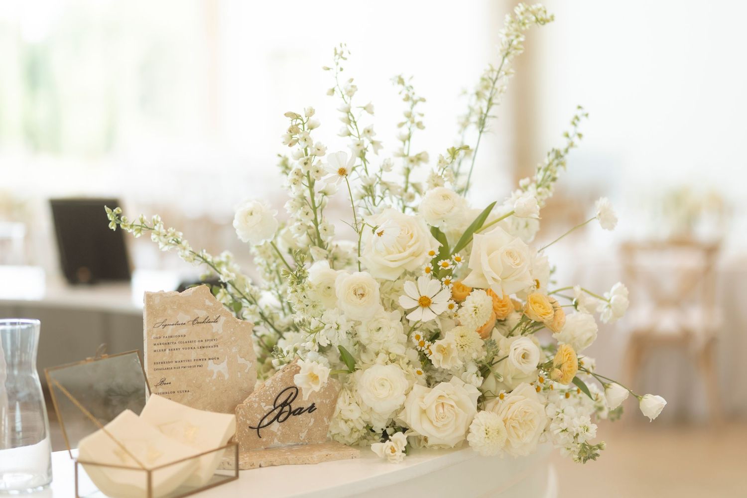 White floral arrangements with delicate blooms and greenery decorate a light-filled event space.