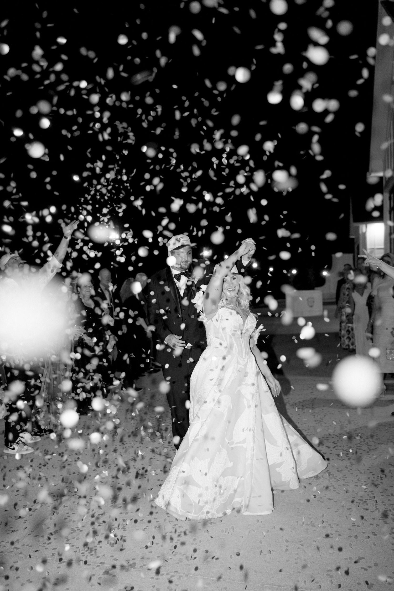 Black and white photo of snow falling during nighttime wedding celebration.