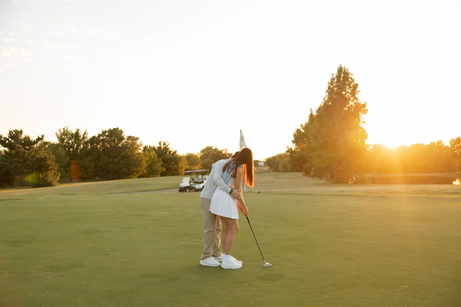 Golfer practicing their putting stance on a golf course during sunset.