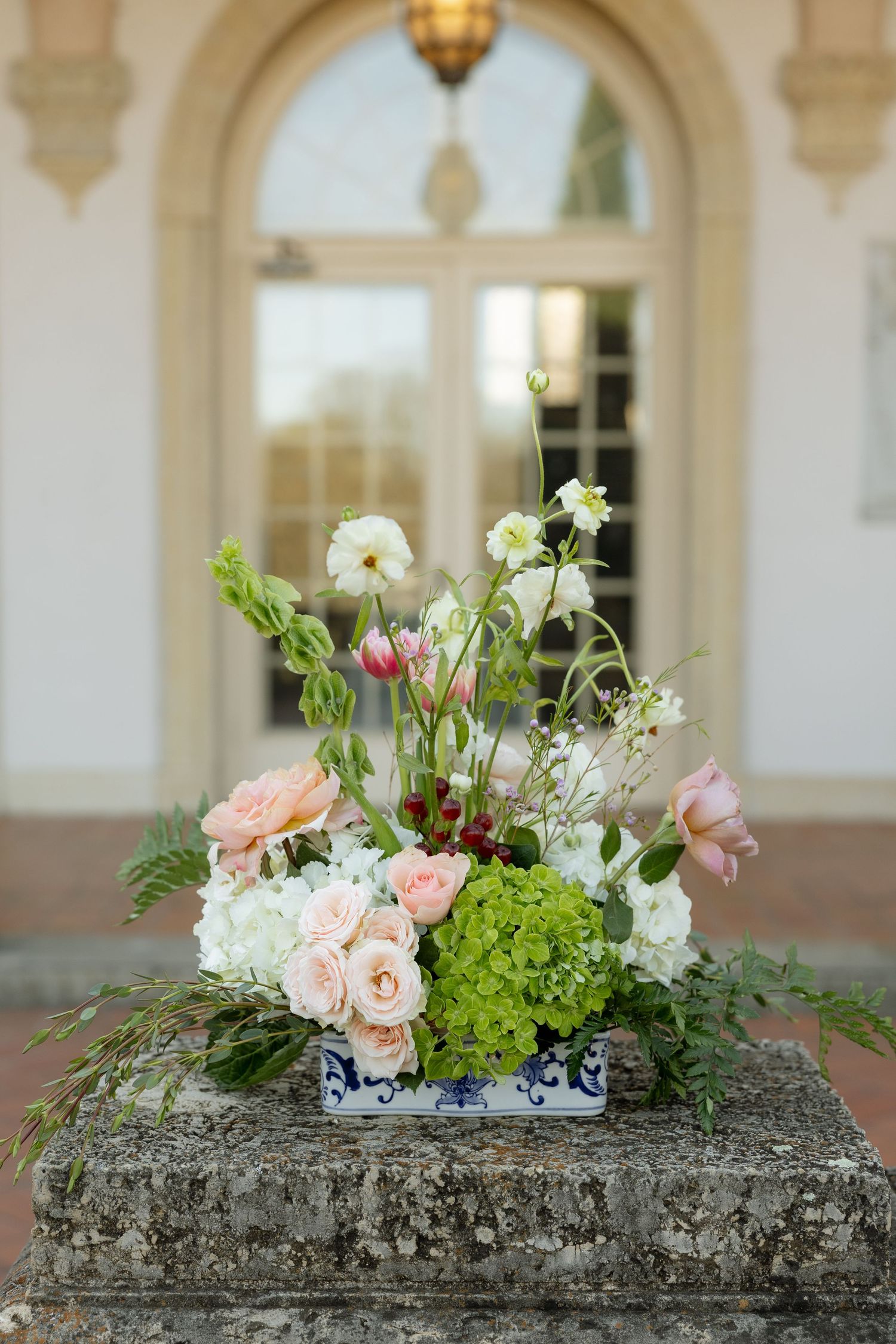 Elegant floral arrangement of pink roses, hydrangeas, and wildflowers on stone pedestal.