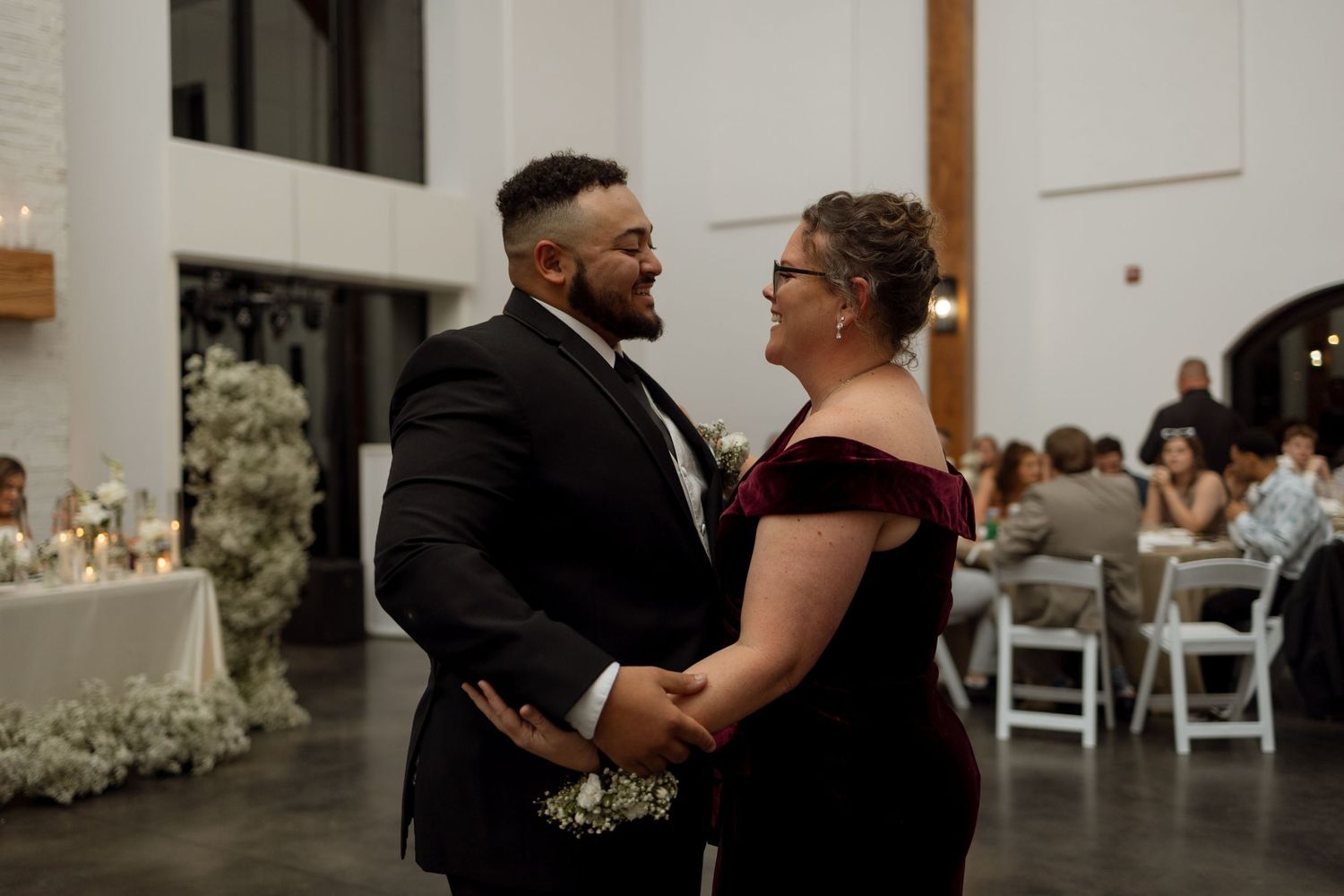 A touching dance moment between wedding attendees in formal attire within an elegant reception venue.