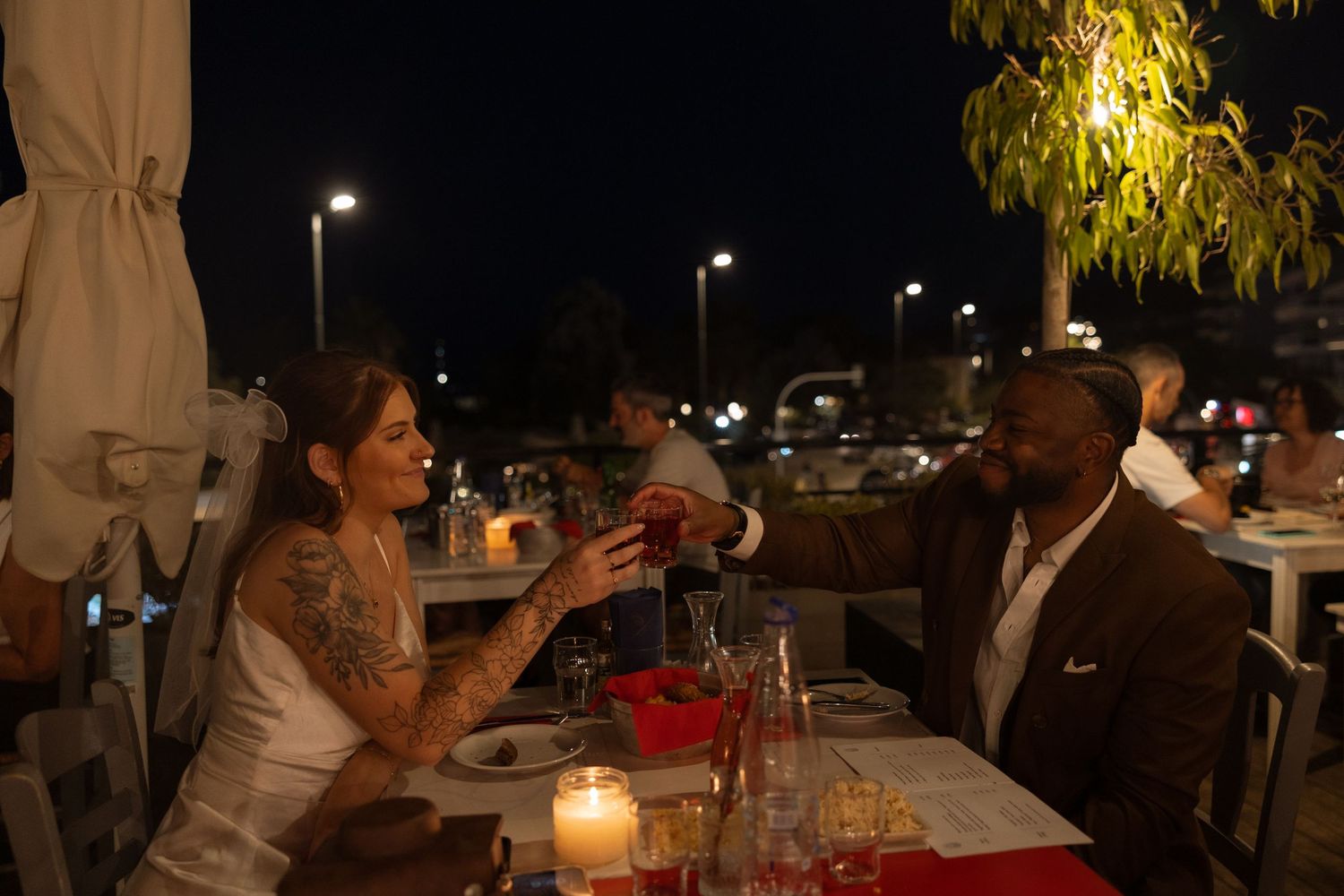 Couple dining at a romantic candlelit outdoor restaurant table at night.
