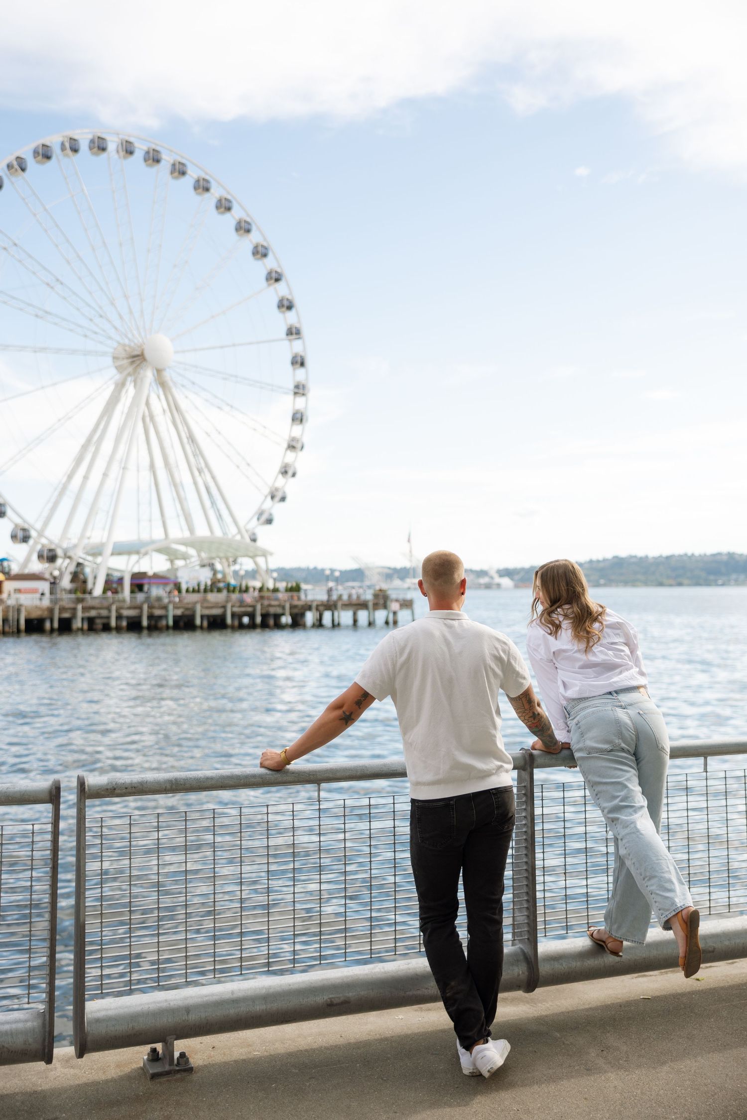 Couple leaning on railing overlooking Seattle waterfront and Great Wheel.