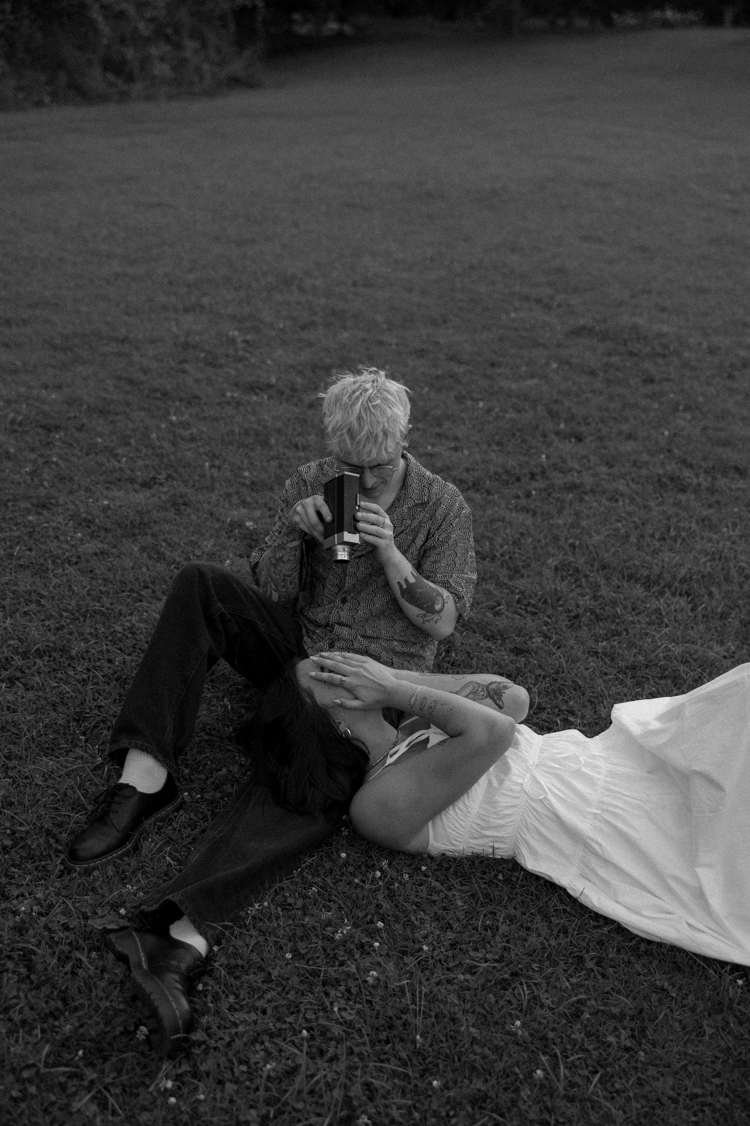 Black and white photo of two people resting on grass during a casual outdoor photoshoot.