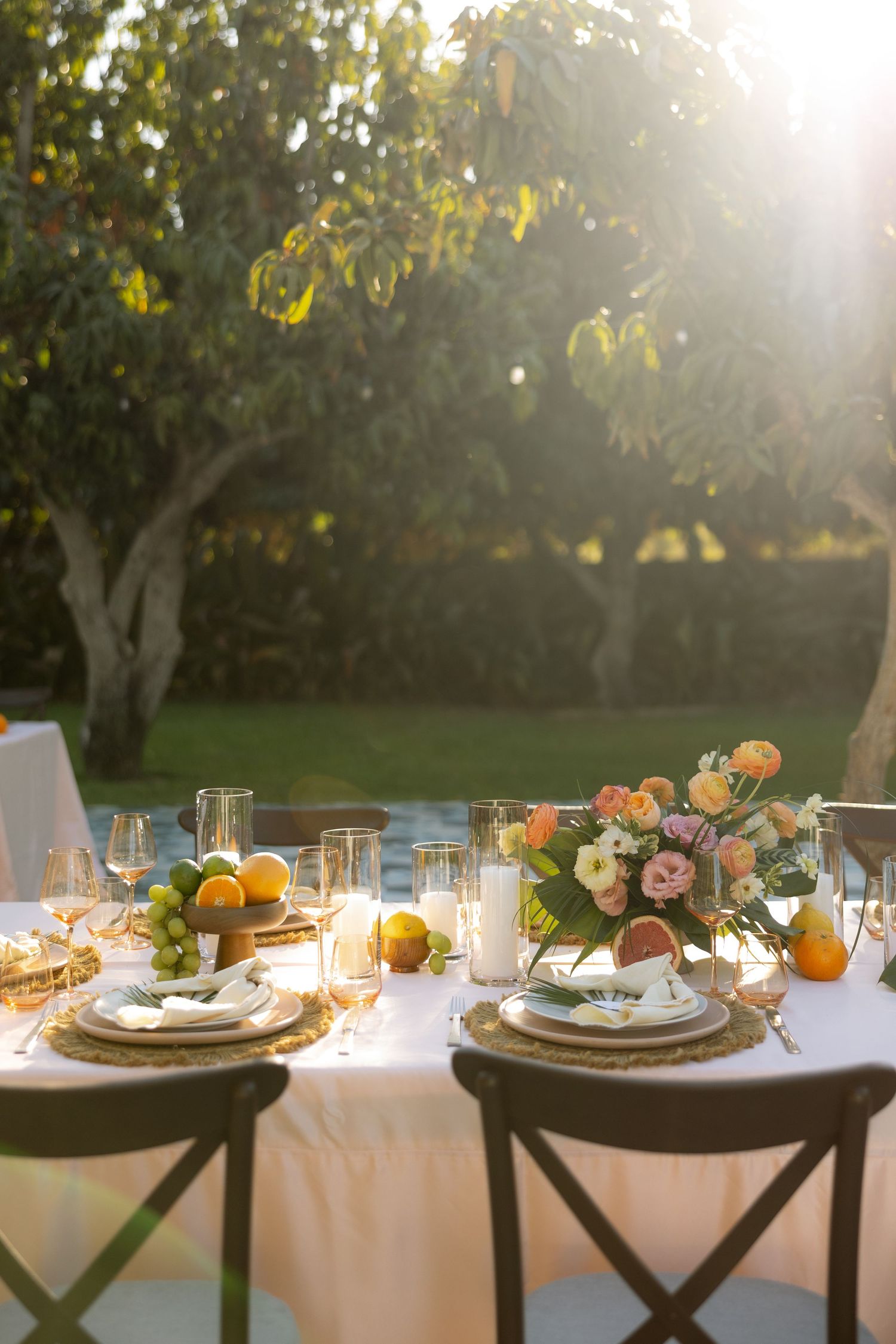 Outdoor wedding reception table set with citrus centerpieces and floral arrangements at sunset.