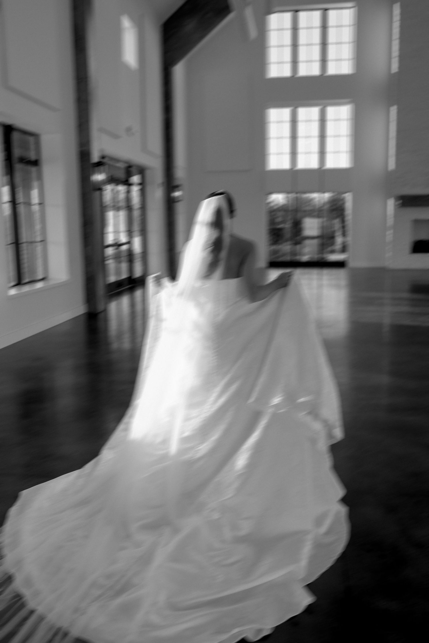 Blurred motion shot of a bride in a flowing wedding gown with long train walking through a hall.