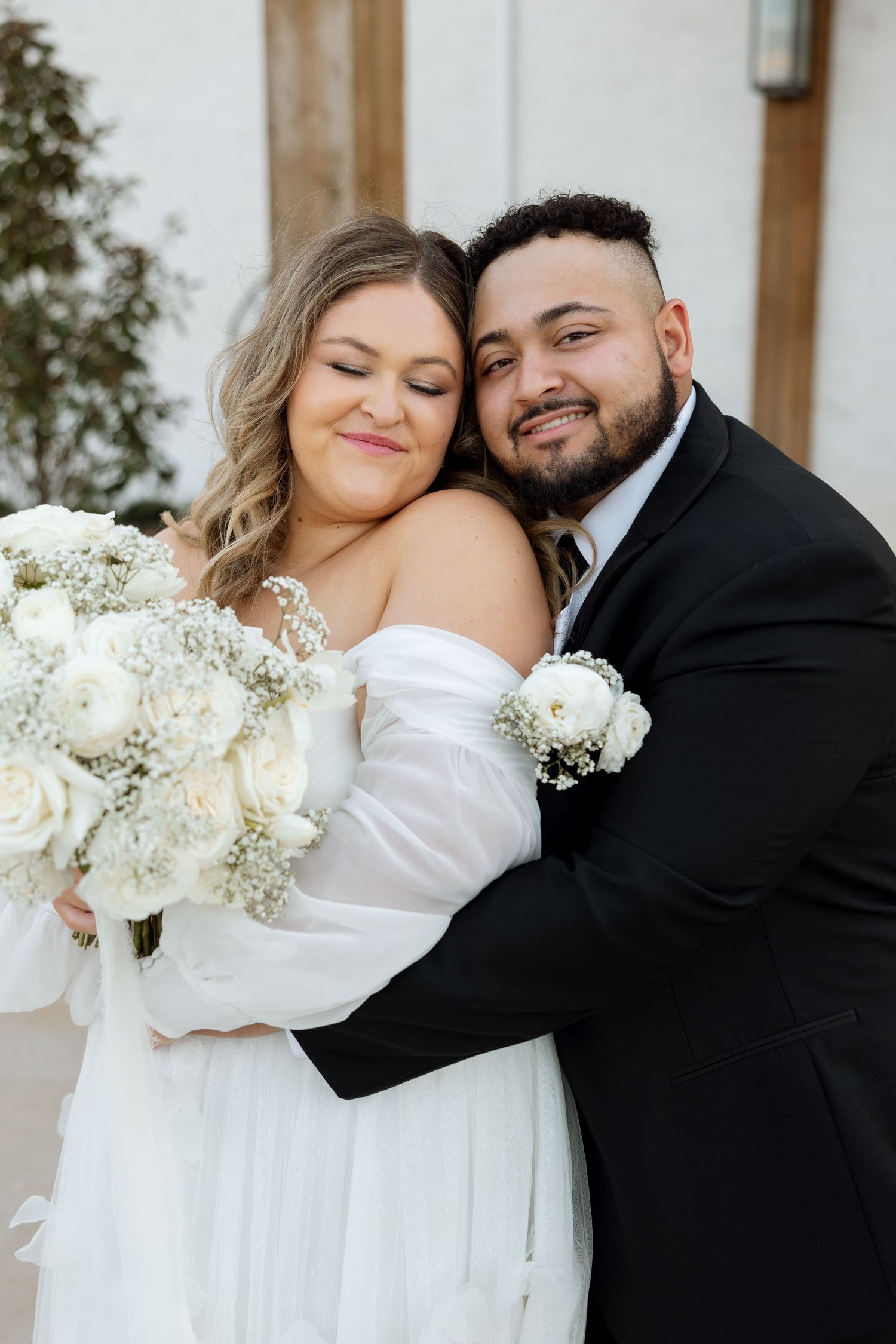 A romantic close-up wedding portrait featuring white floral bouquet and intimate embrace.