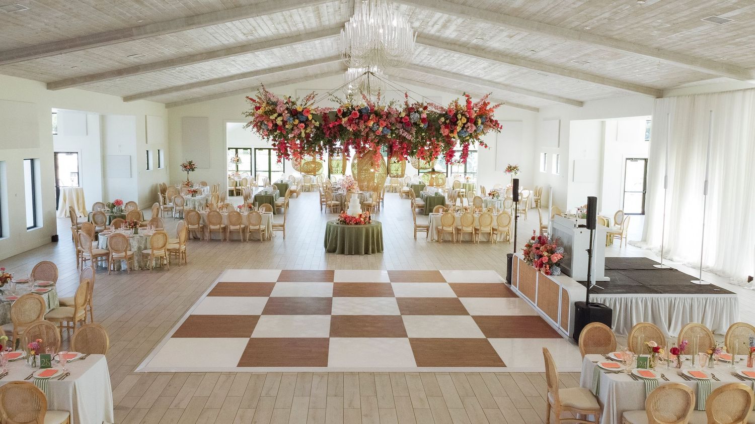 Panoramic view of an elegant white wedding reception hall with checkered floor and hanging floral decorations.
