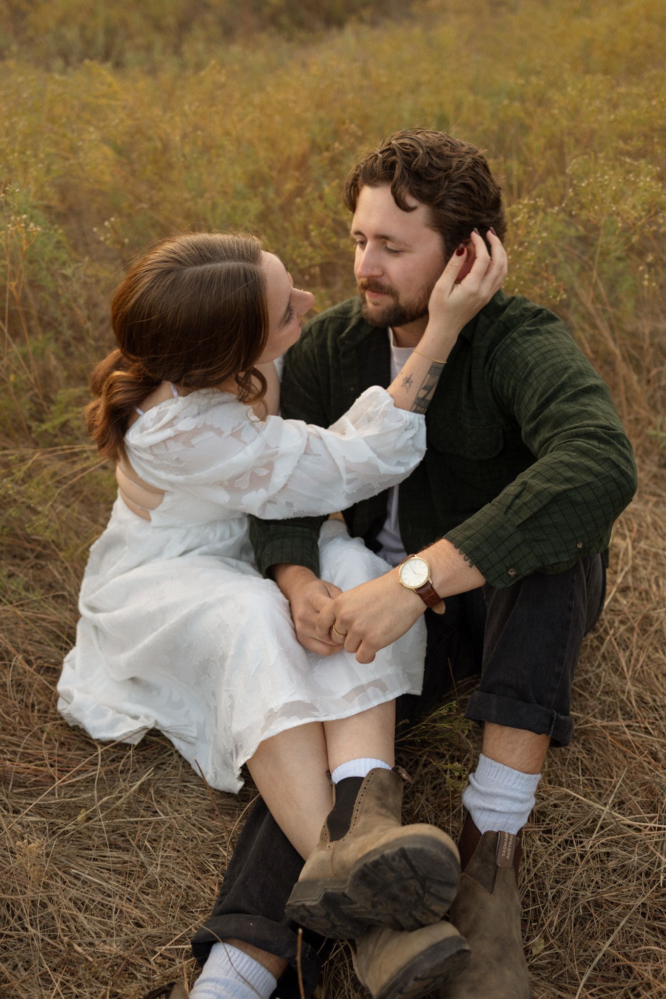 A couple sits intimately in a fall meadow wearing contrasting white dress and dark jacket.