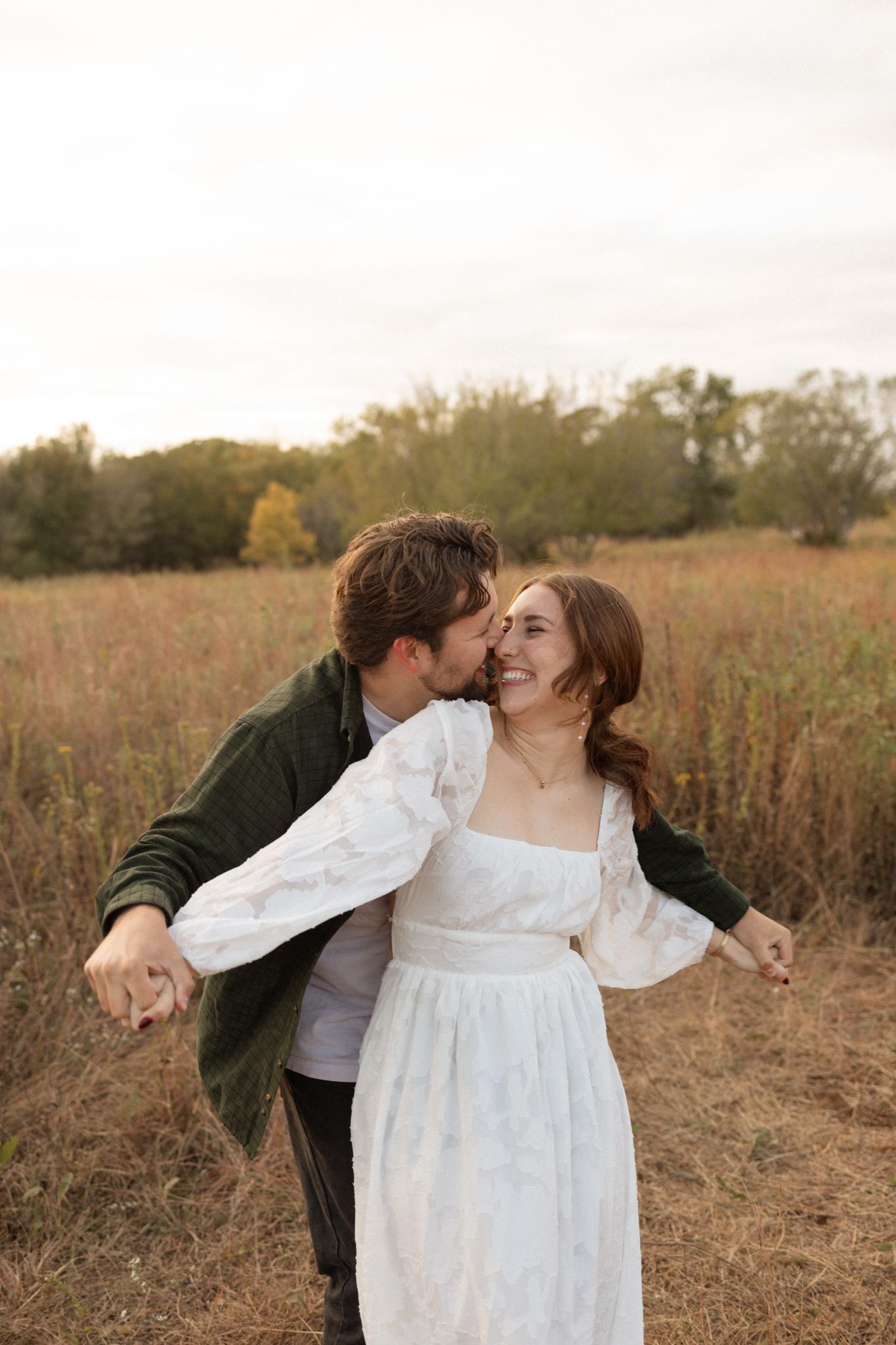 Couple embraces lovingly in autumn field during sunset photo session.