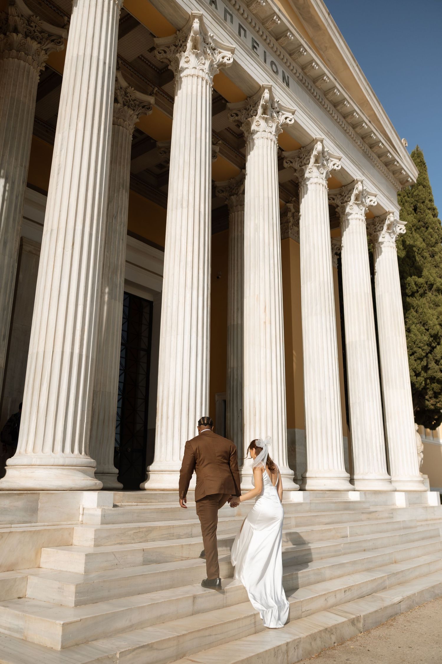 Couple ascends grand staircase of historic building with towering columns.