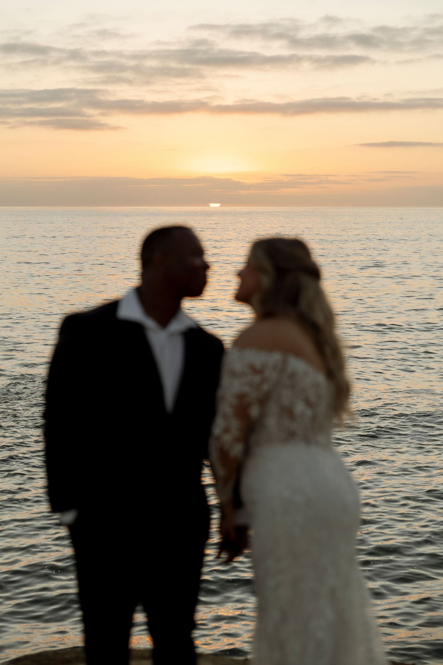 Silhouettes of a wedding couple embrace against a golden sunset over the ocean.