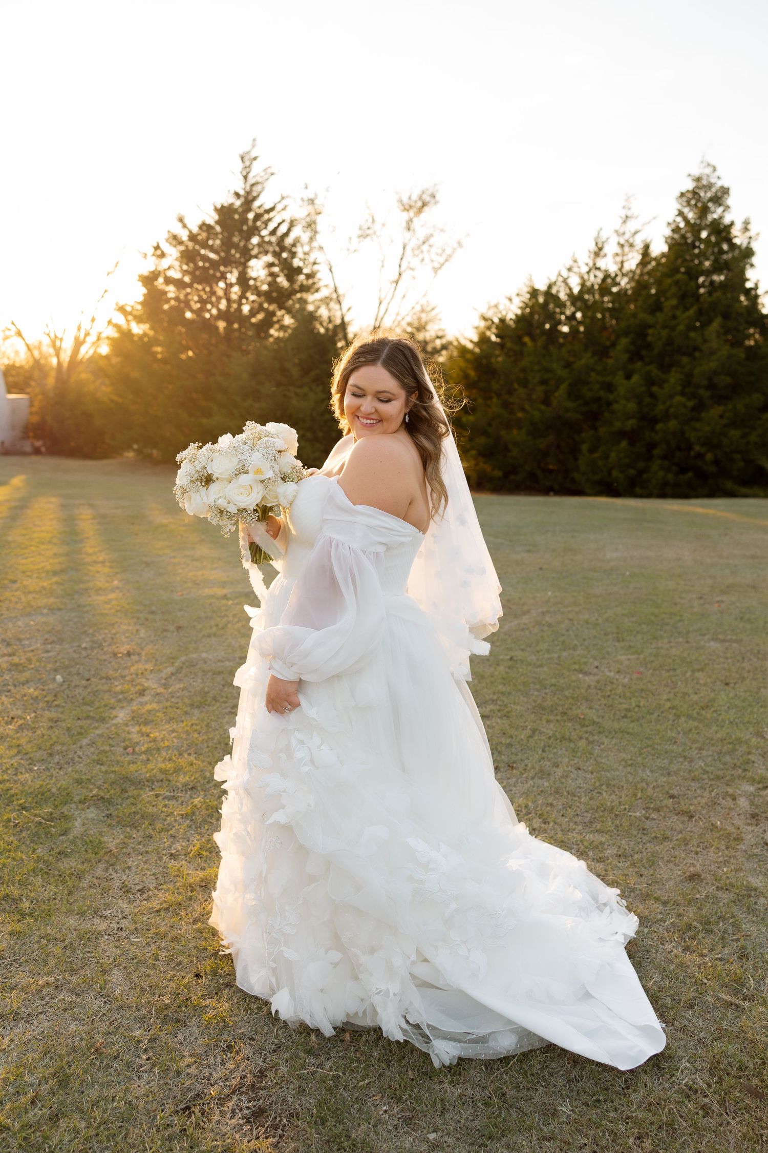 A bride in a flowing white gown poses with her bouquet during golden hour.