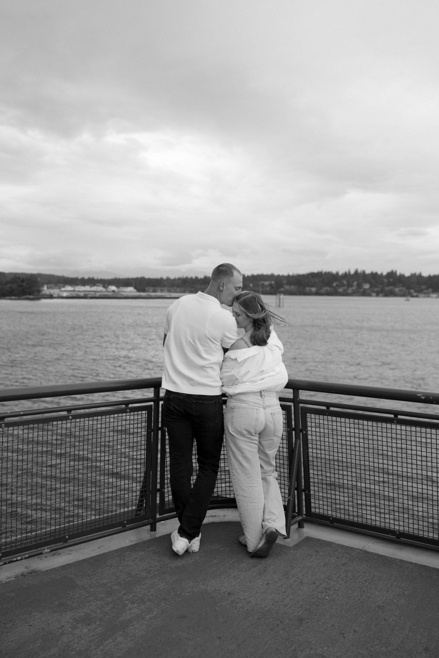 A couple in white attire standing together at the railing of a ferry deck overlooking the water.