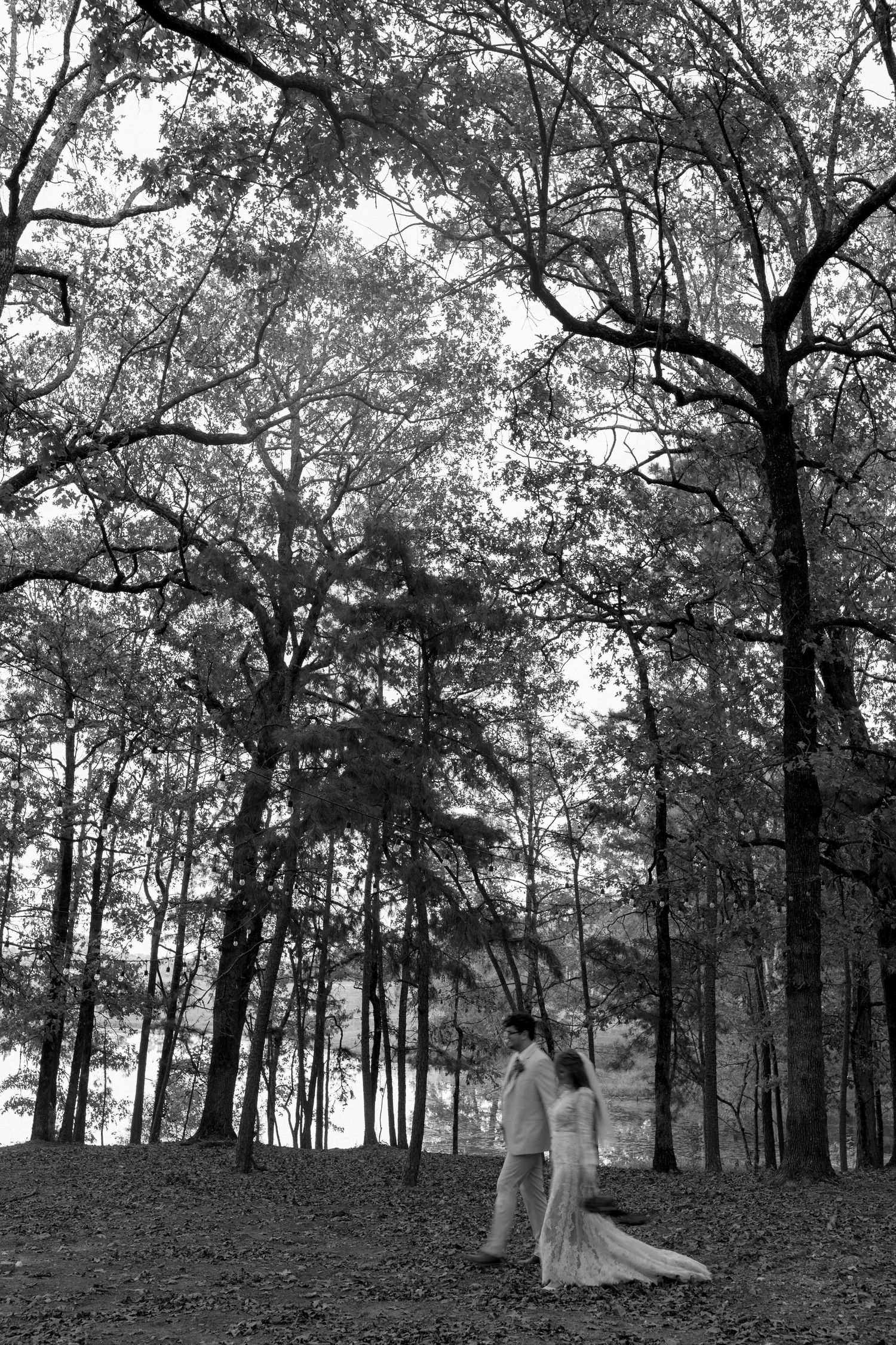 A black and white wedding photo of a couple standing together in a tranquil wooded setting.