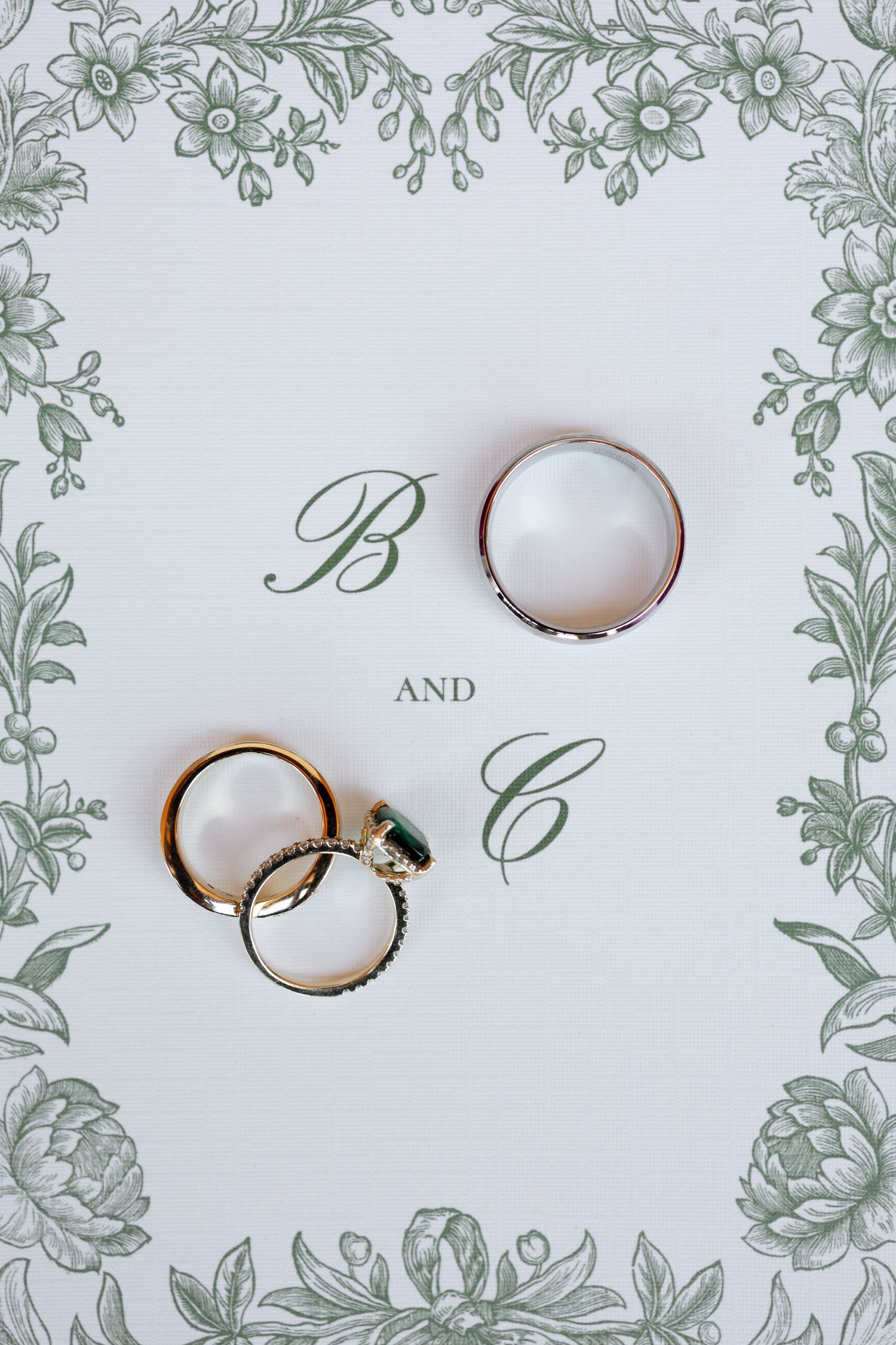 Wedding rings photographed on white invitation with elegant green floral border design.