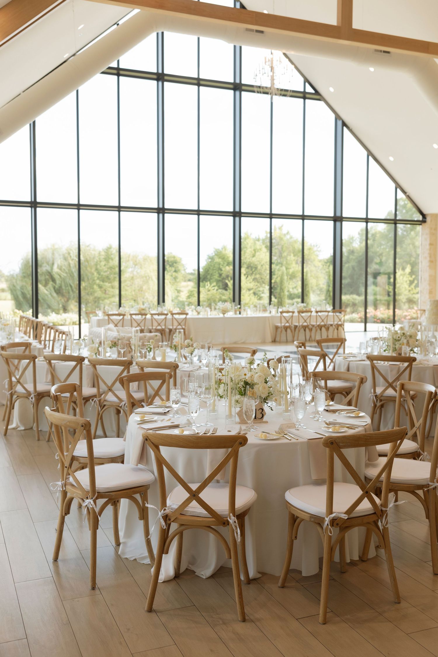 Modern wedding reception venue with wooden cross-back chairs and floor-to-ceiling windows.
