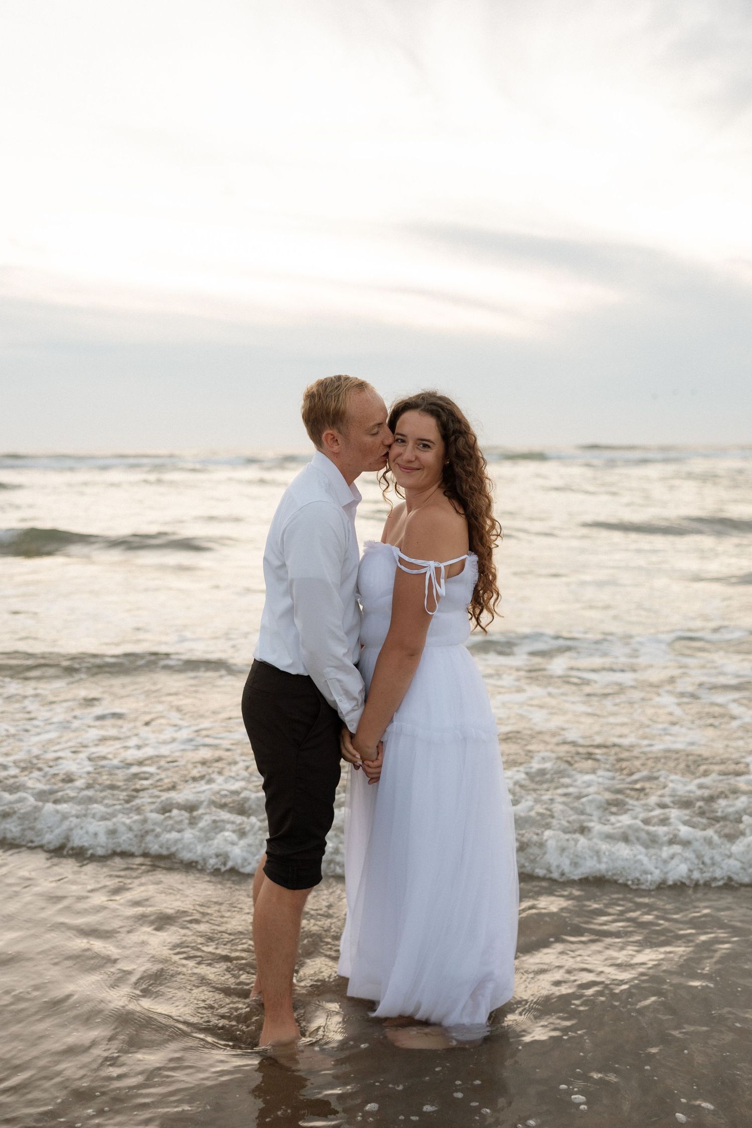 A tender moment between newlyweds on the beach at sunset with waves crashing behind them.