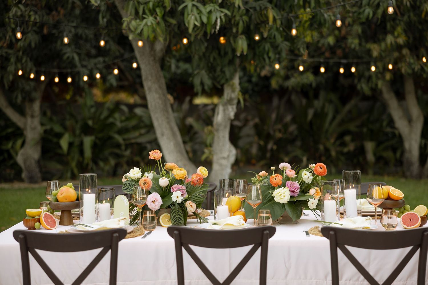 Romantic outdoor wedding reception table with colorful floral centerpieces and string lights at dusk.