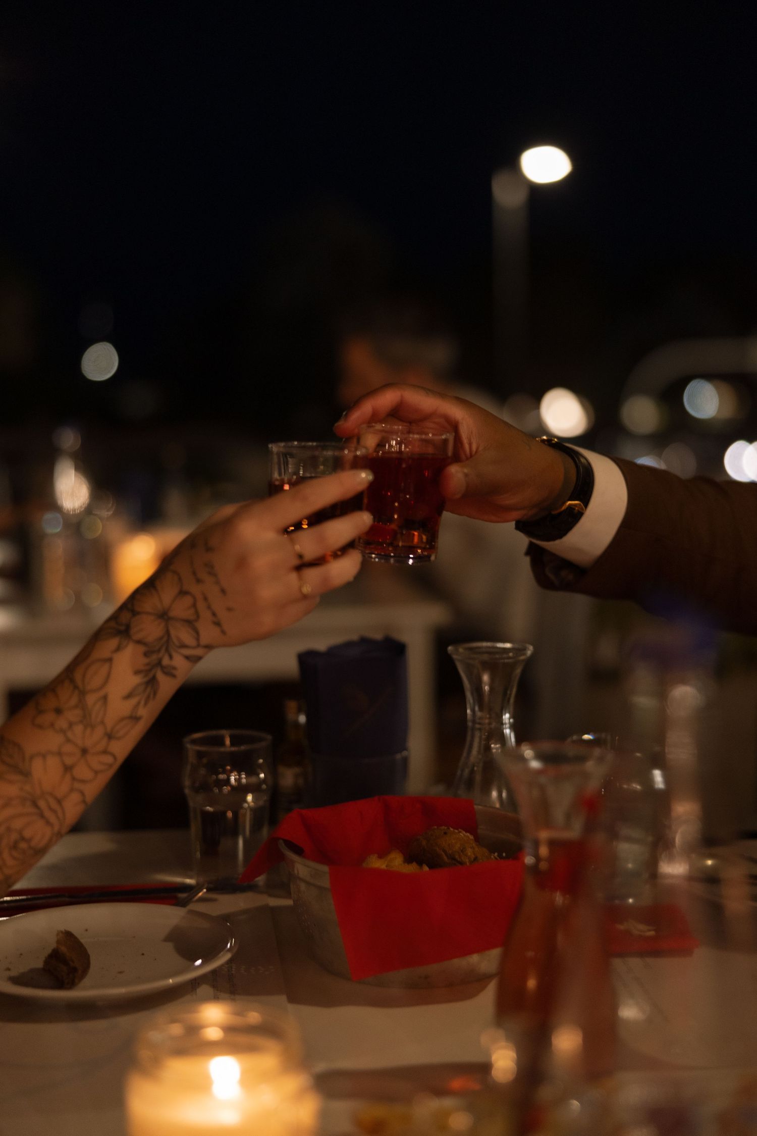 Hands toasting drinks across a candlelit dinner table with glasses.