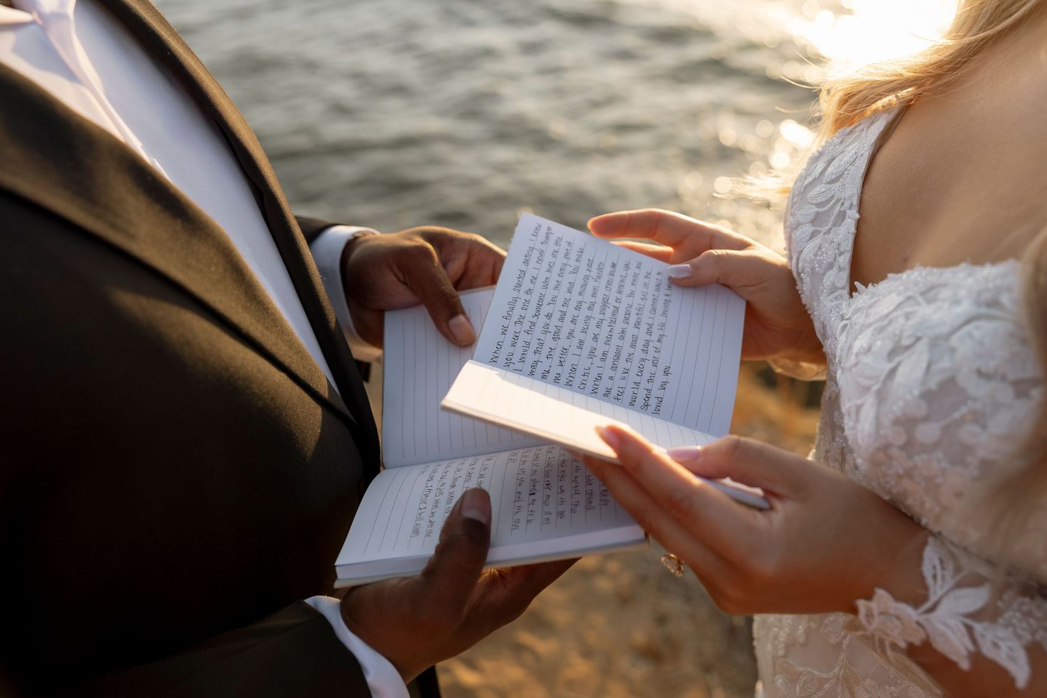 Close-up of hands holding wedding vow books during an outdoor ceremony by the water.