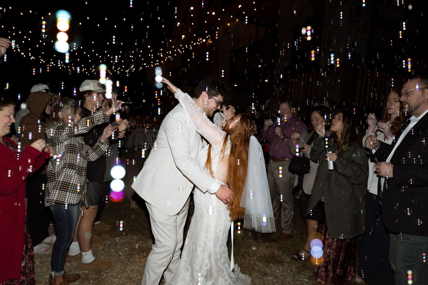 Newlyweds share a kiss surrounded by guests with sparklers at their reception exit.