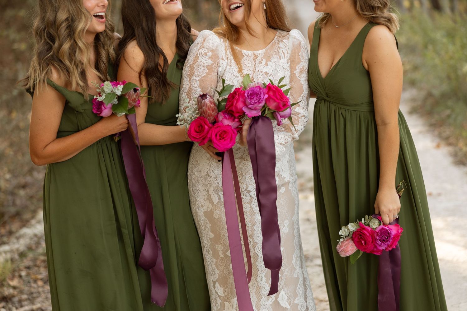 Close-up of wedding party with green dresses and pink bouquets sharing candid moment.