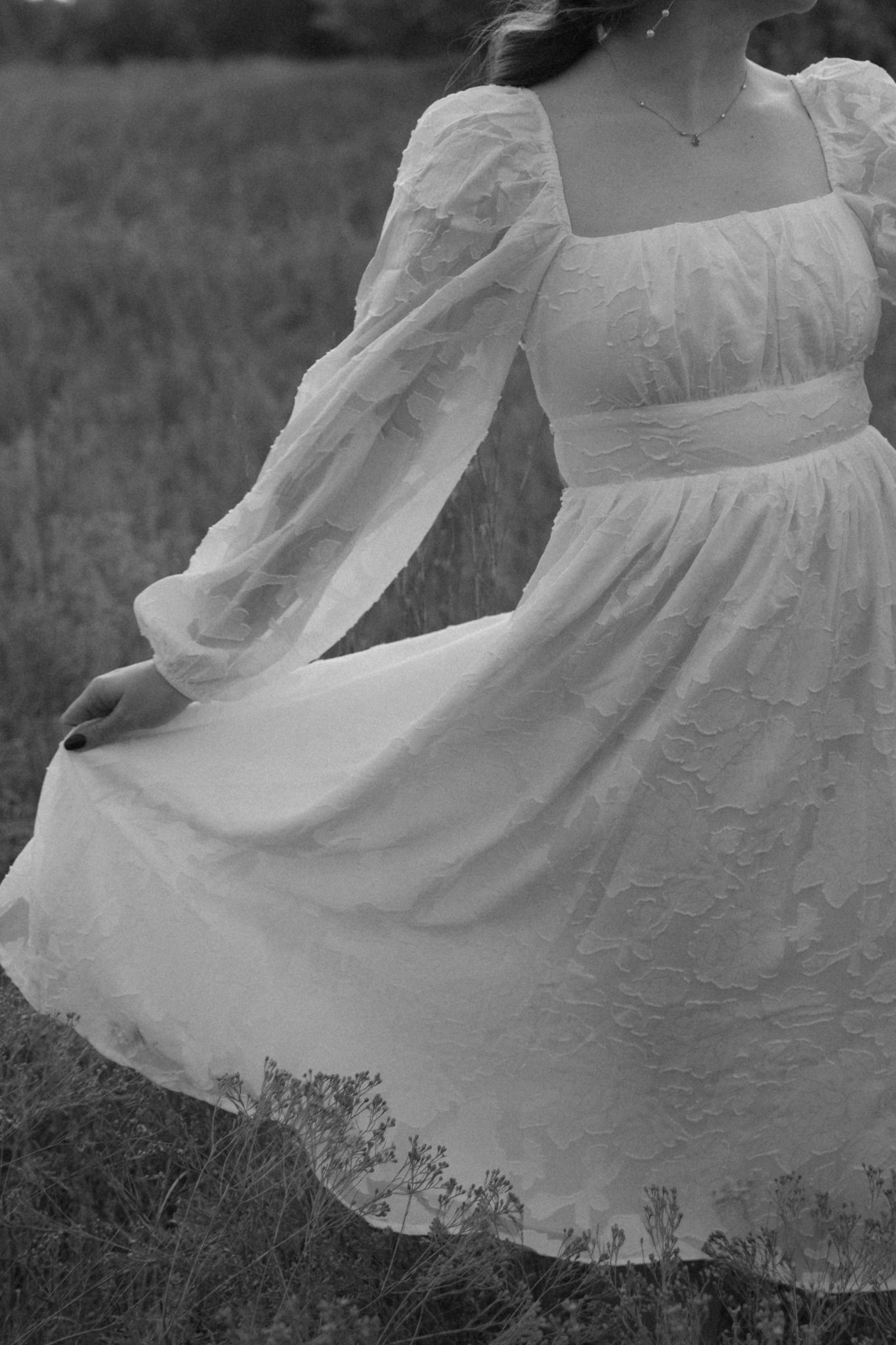 A black and white photo shows a flowing white dress with puff sleeves twirling in a field.