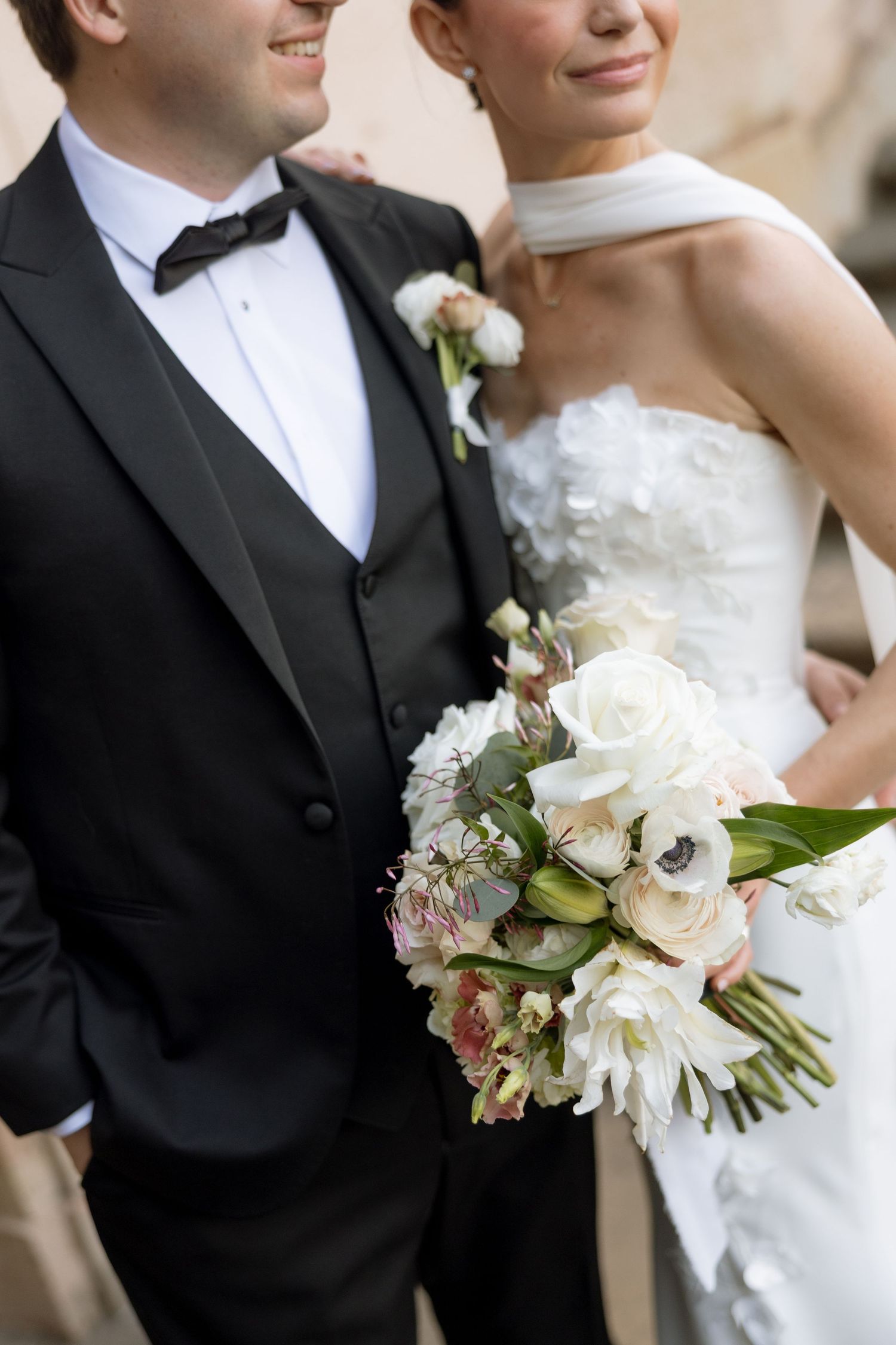 Bride holding white and blush floral bouquet beside groom in black tuxedo on wedding day.