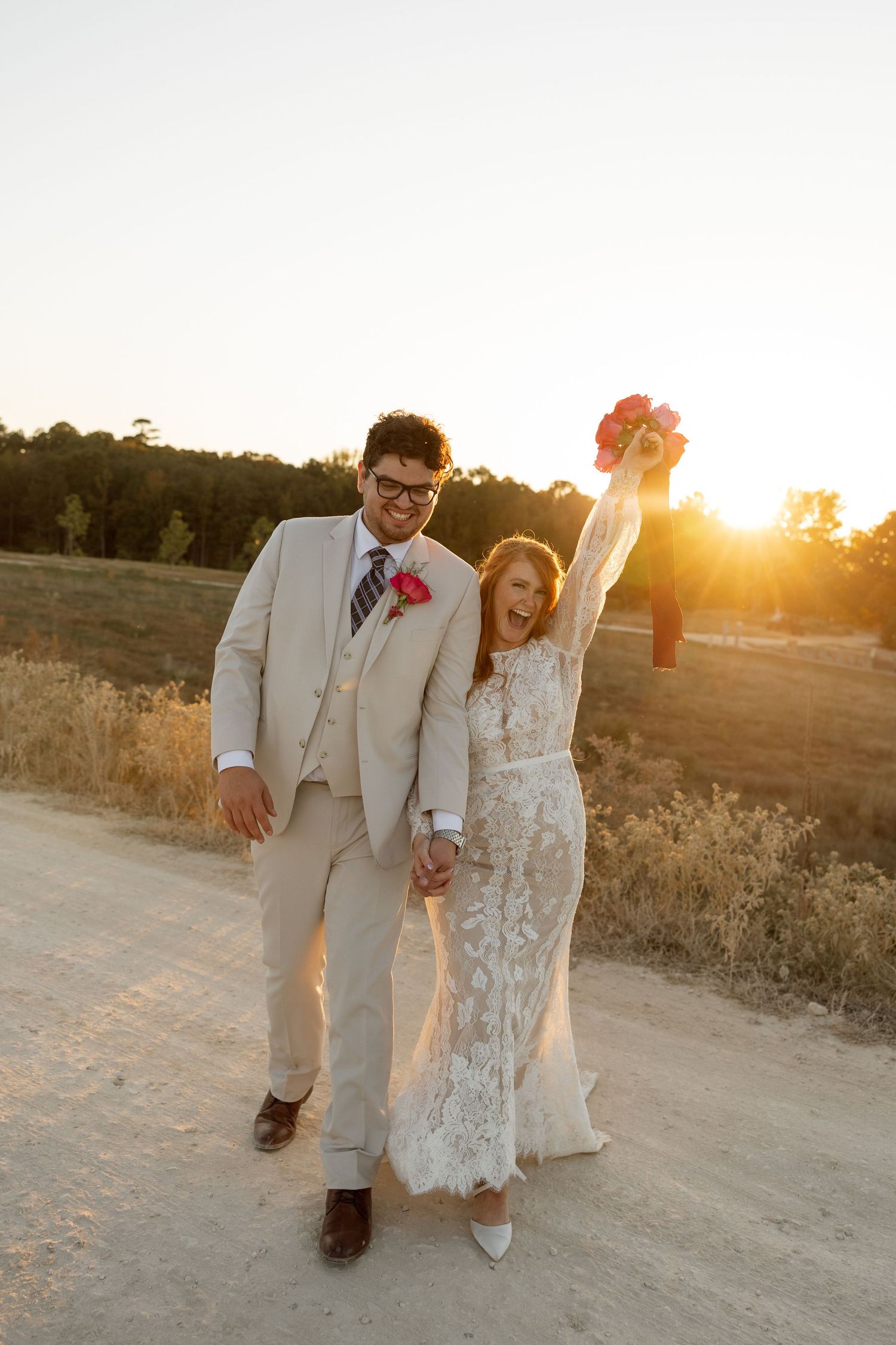 An energetic sunset wedding photo showing a celebratory moment on a country path.