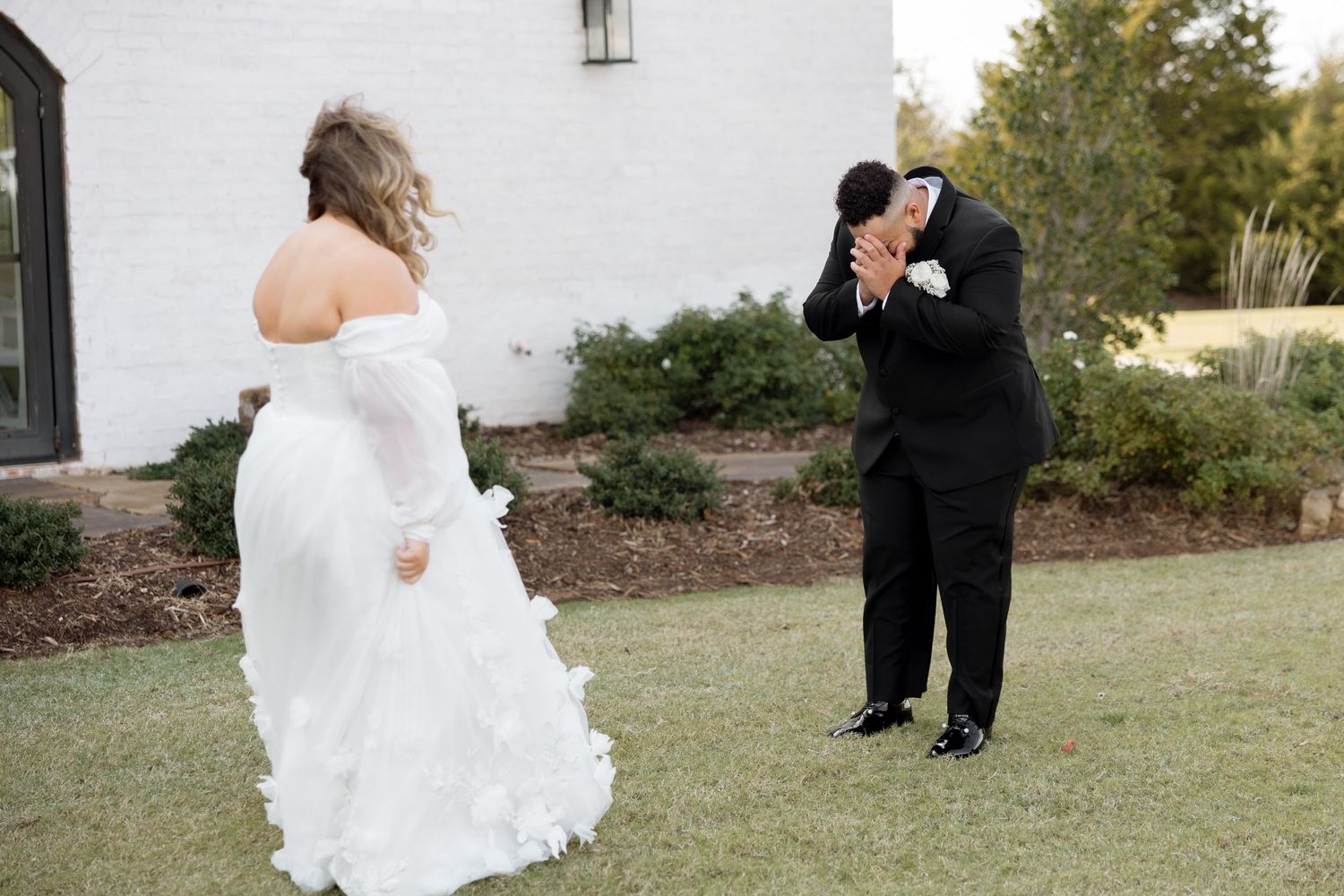 Intimate first look moment captured between couple in formal wedding attire outside white building.