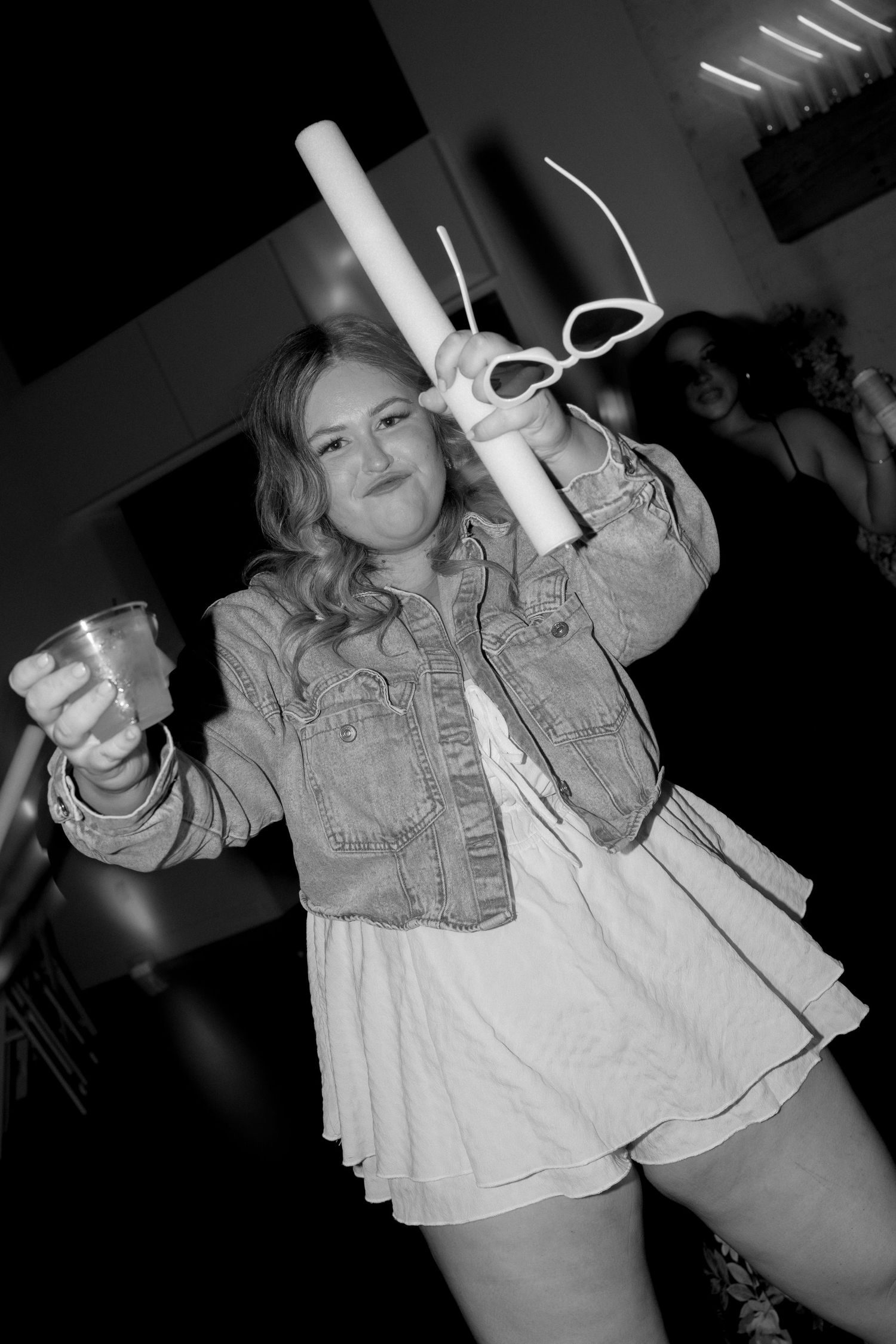 Guest dancing at wedding reception wearing denim jacket and holding glow sticks in black and white.