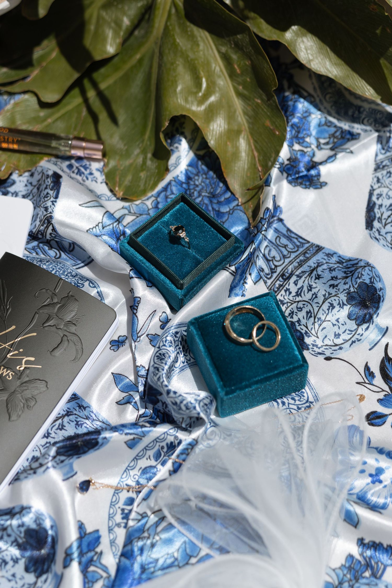 Wedding rings in teal velvet ring boxes on blue and white patterned fabric.