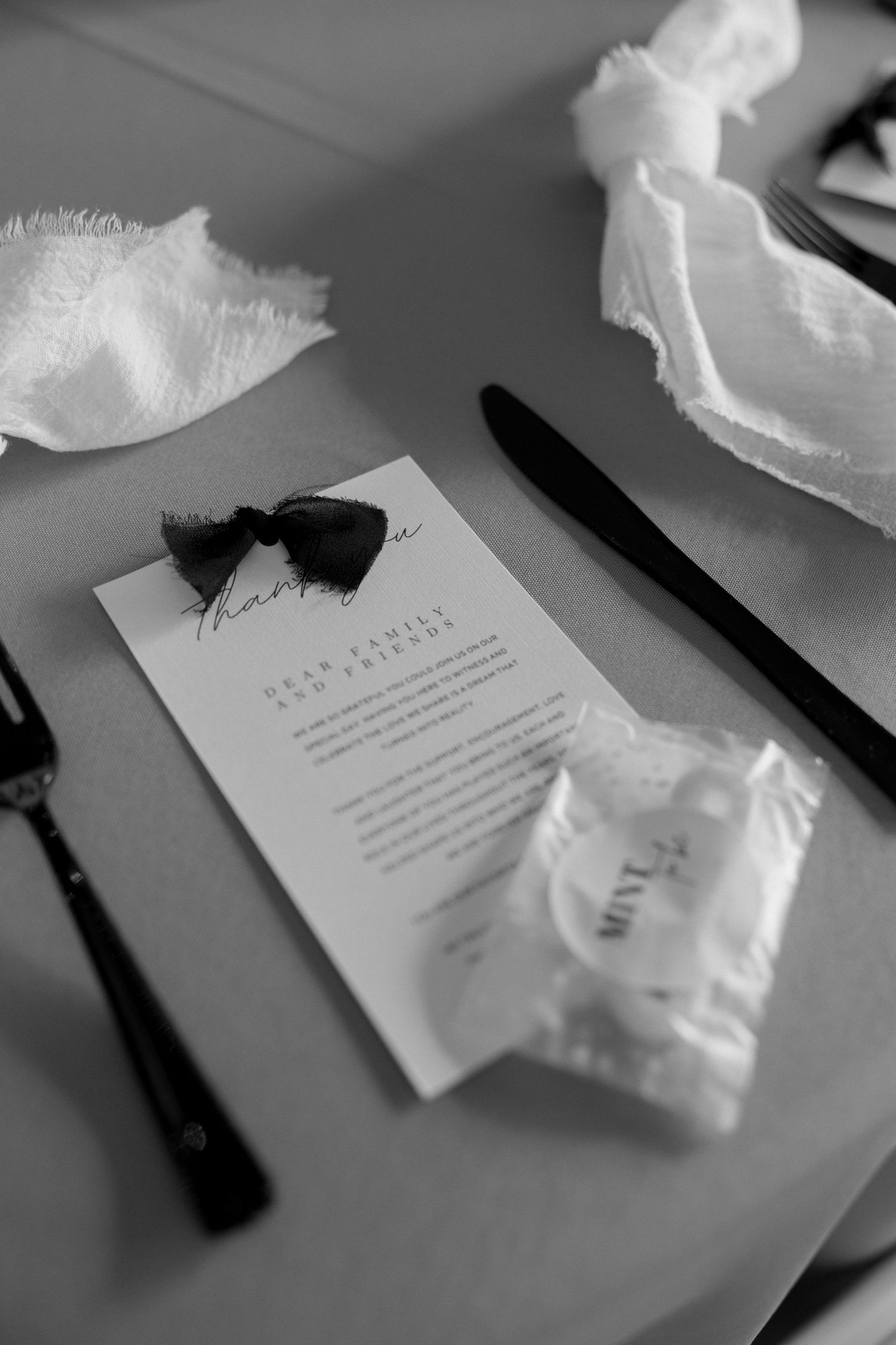 Black and white detail shot of wedding menu card with tissues and utensils.