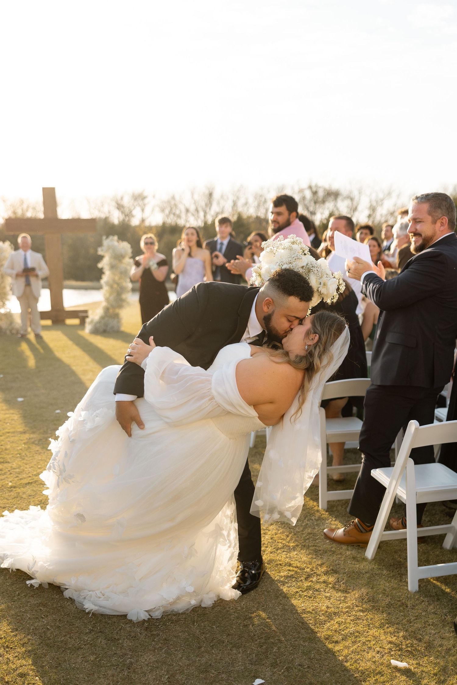 Romantic dip kiss during recessional at outdoor wedding ceremony with guests applauding.