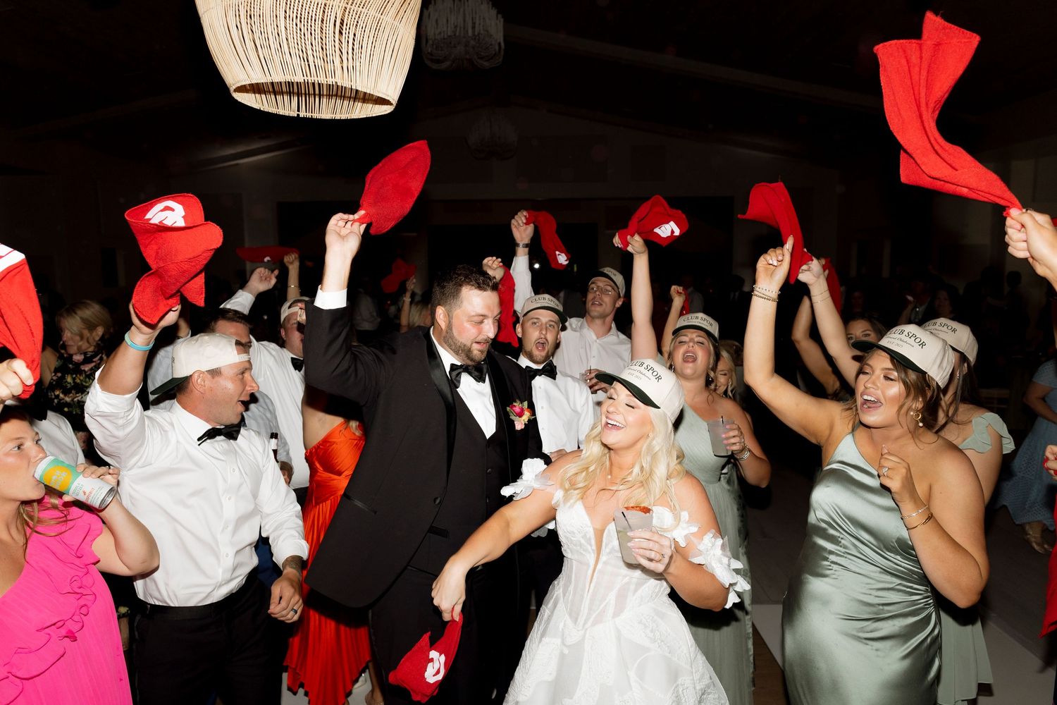 Wedding guests wave red napkins during a reception celebration while dancing on the dance floor.