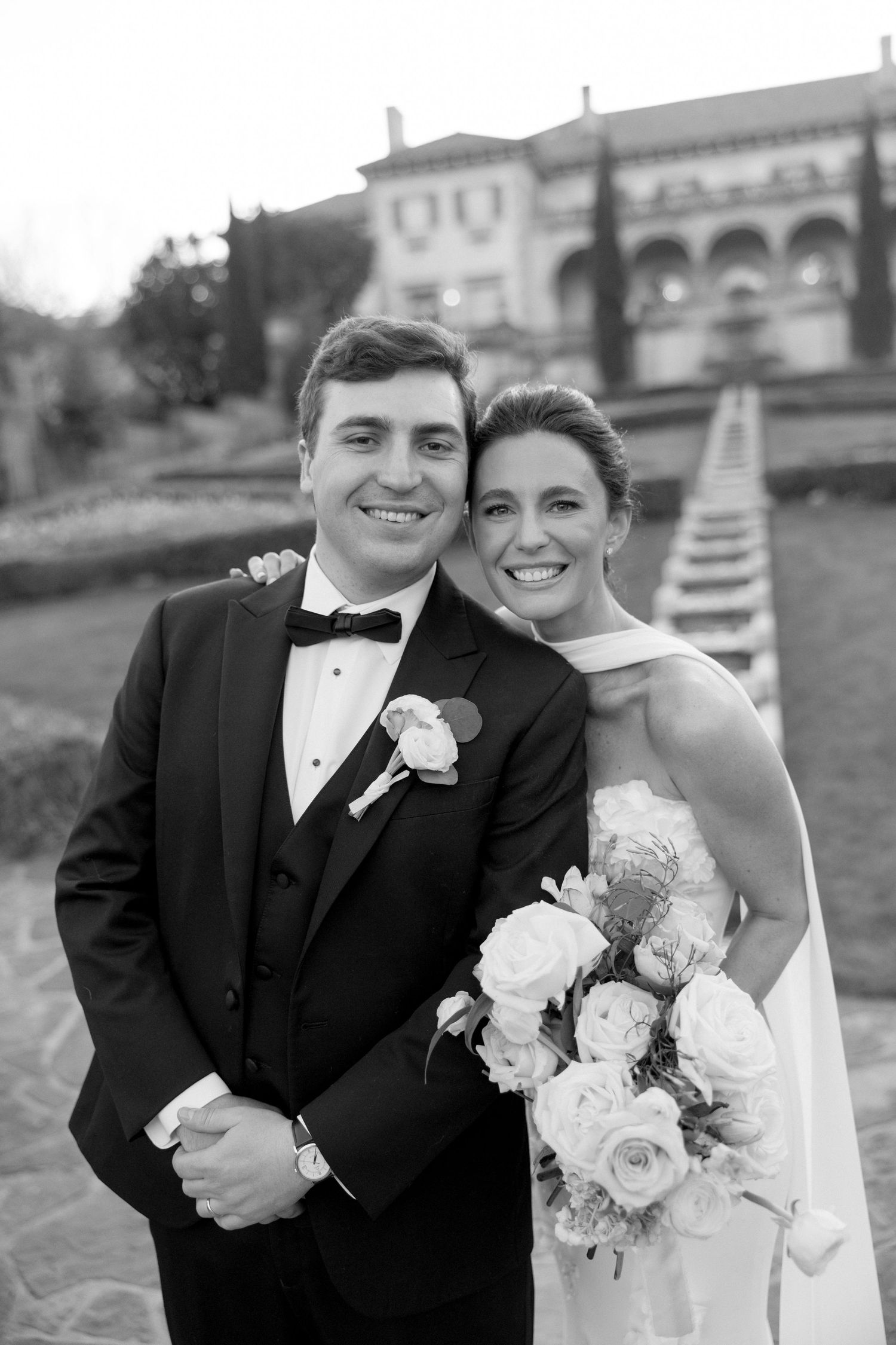 Black and white portrait of smiling bride and groom posing together outdoors at elegant estate wedding venue.