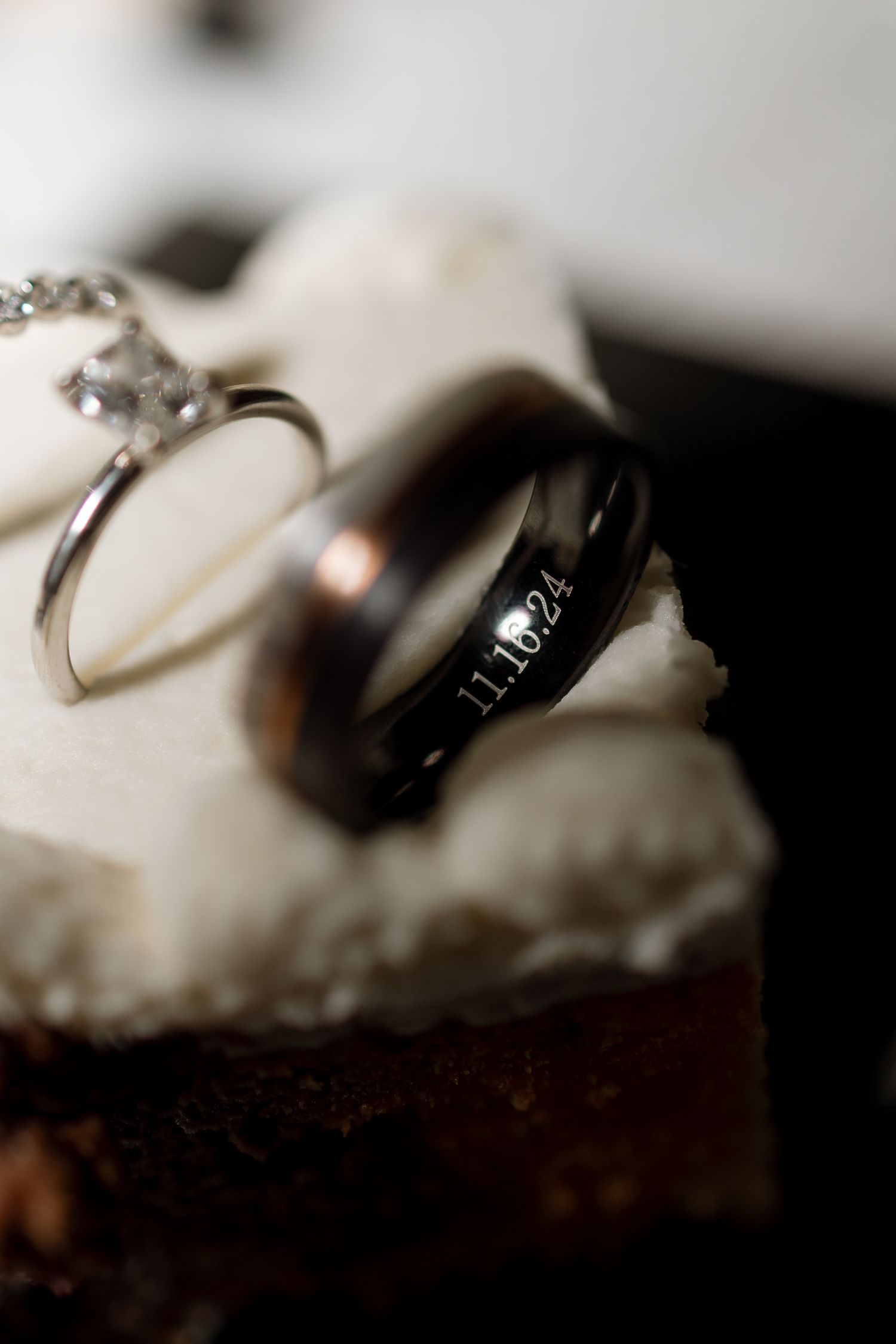 Close-up of wedding rings resting on a dark dessert, showing intricate diamond details.