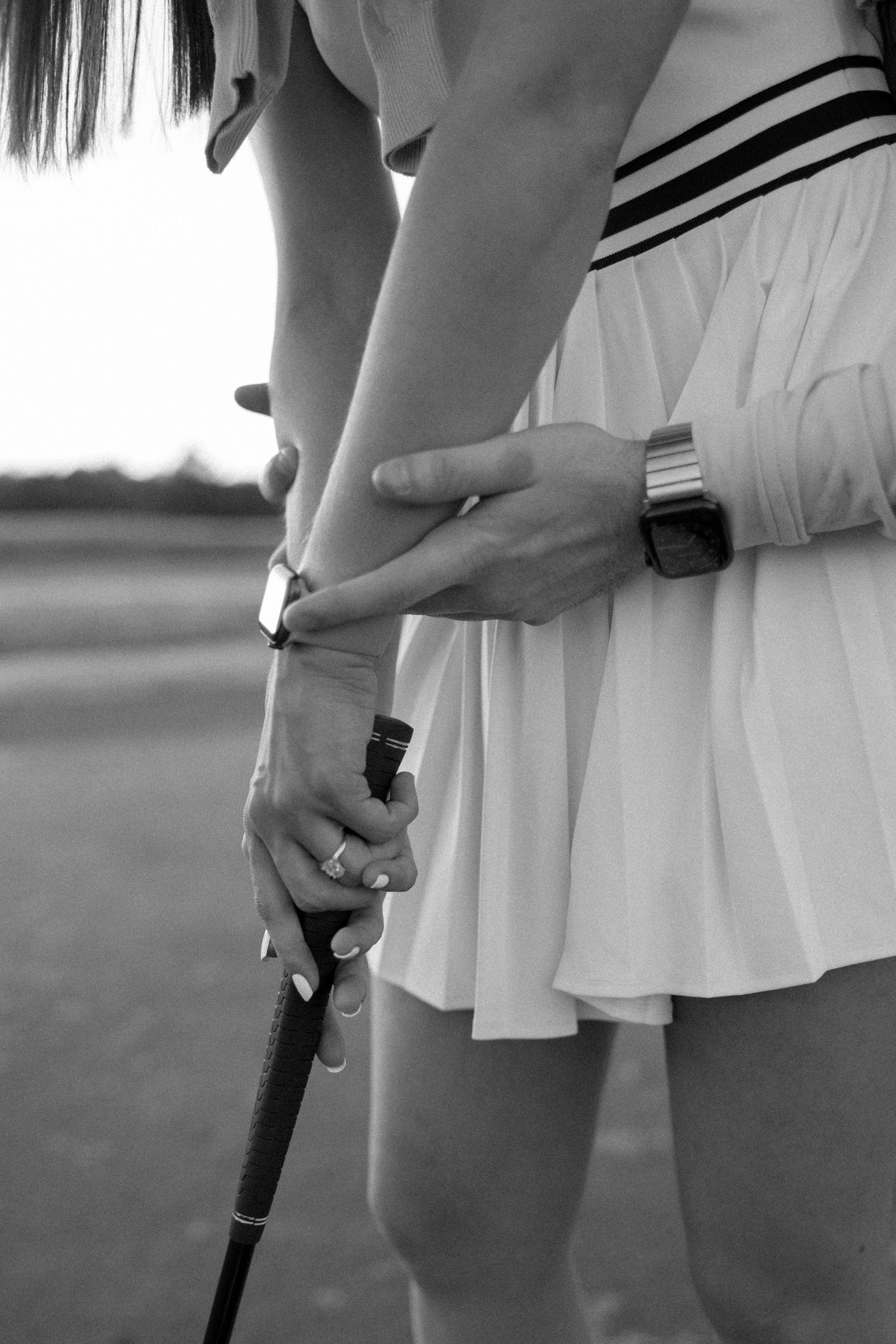 Close-up black and white shot of hands holding a golf club together on a course.