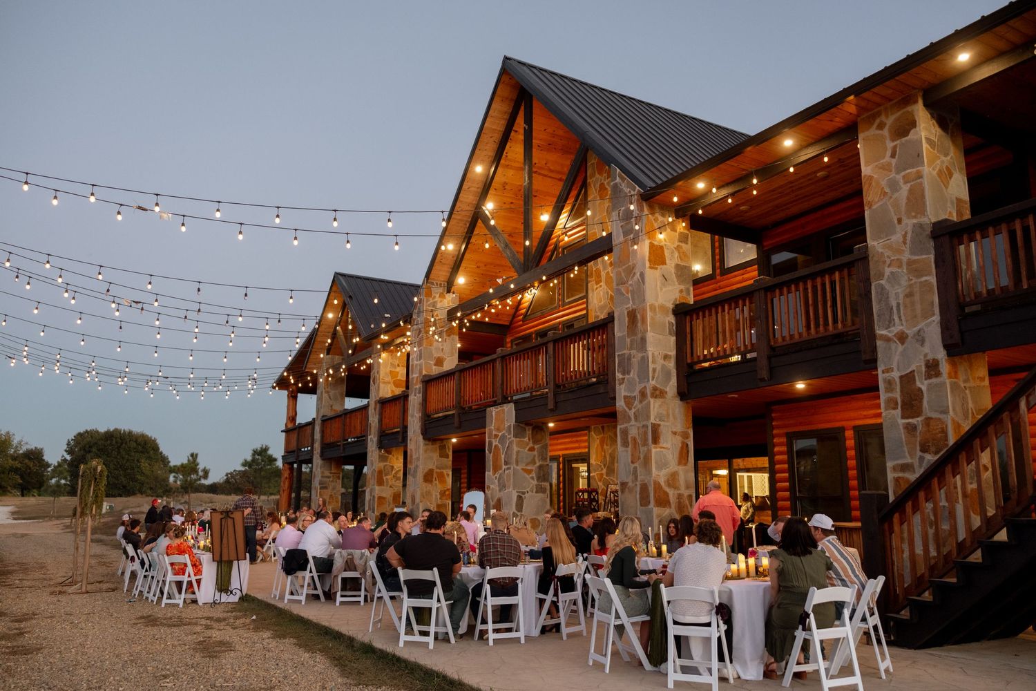 Rustic lodge venue with string lights hosts outdoor wedding reception at dusk.
