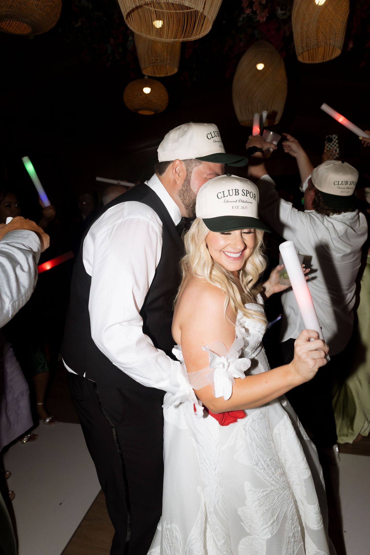 Wedding guests dance and celebrate on a dark dance floor holding colorful light-up glow sticks.