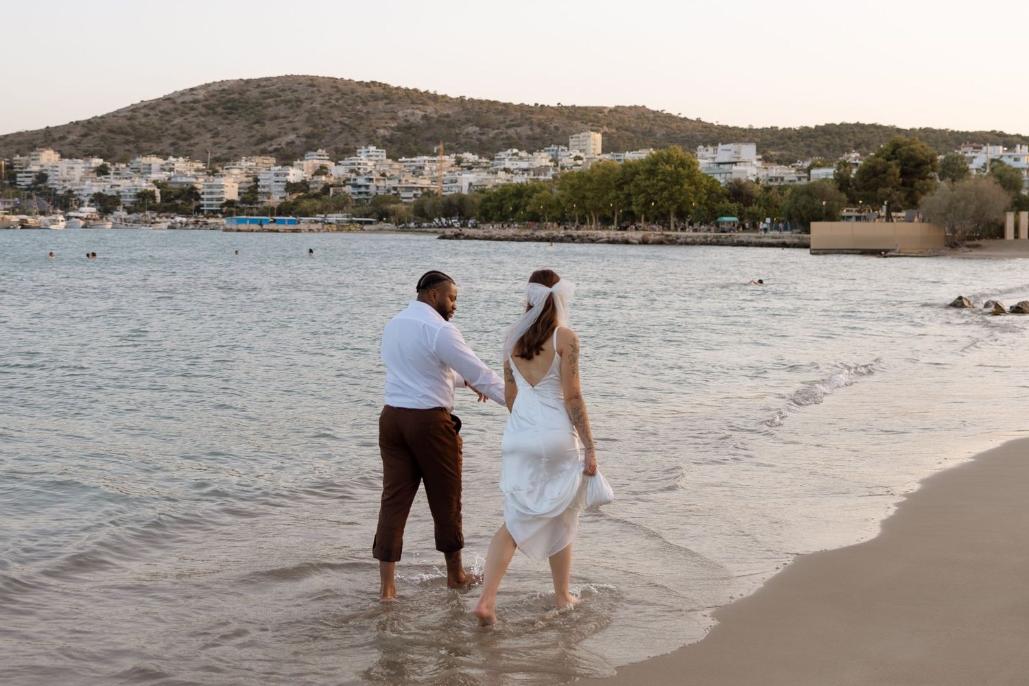 A couple walks hand in hand along a serene Mediterranean beach at sunset.