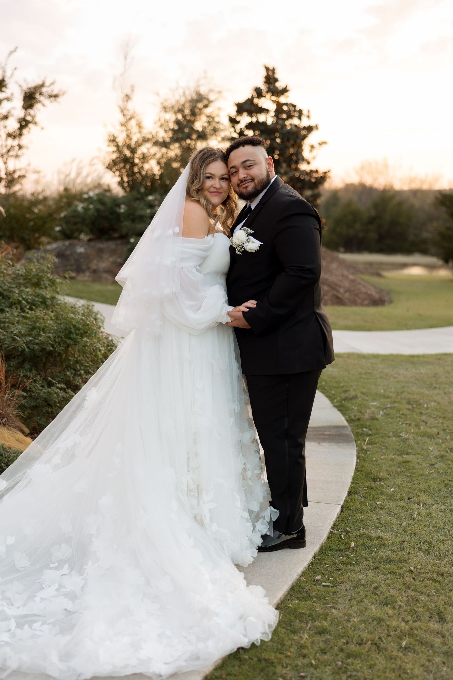 A wedding couple poses on a winding pathway during golden hour.