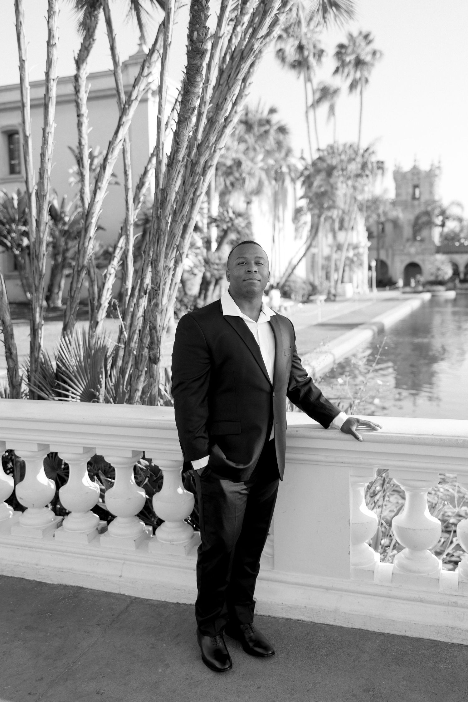 A formal portrait in black and white showing a person in a suit against a palm tree backdrop.