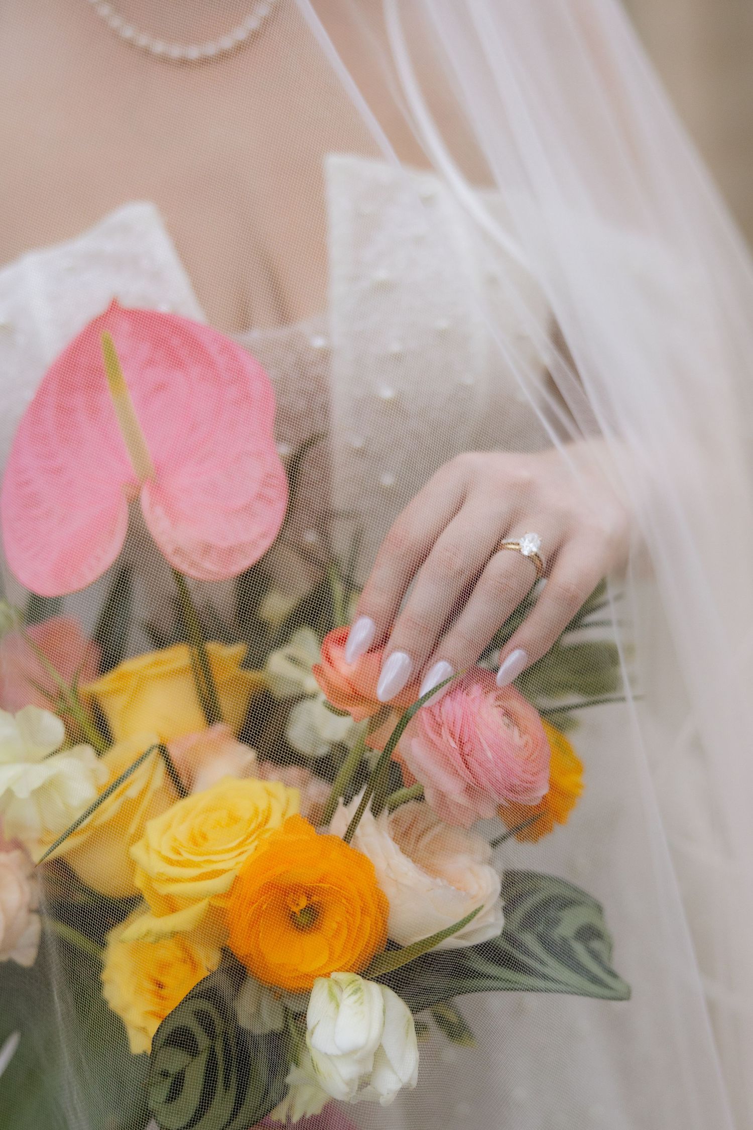 Bride holding a vibrant bouquet of yellow, orange, and pink flowers with a diamond ring on her hand.