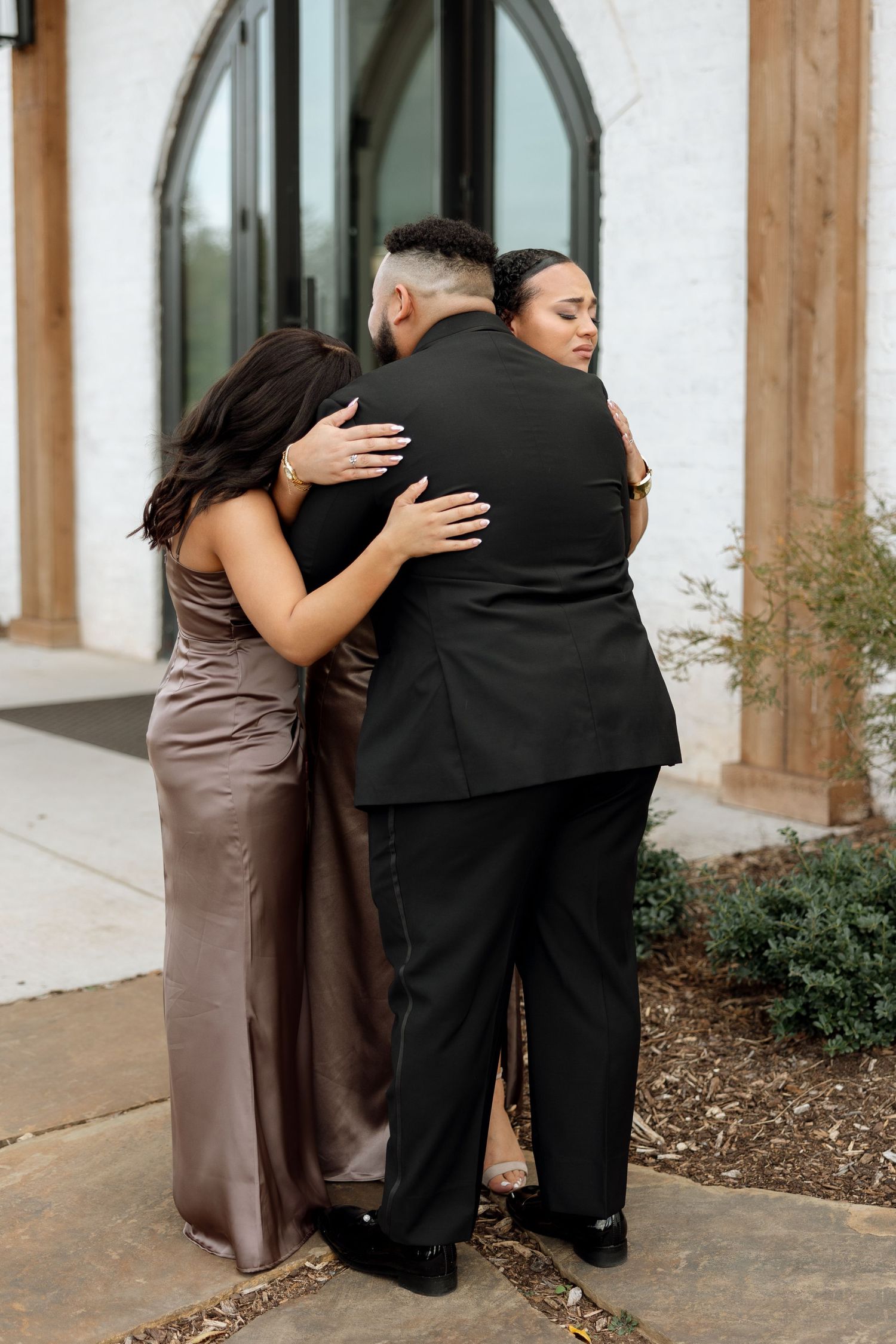 An emotional group hug outside a modern building entrance.