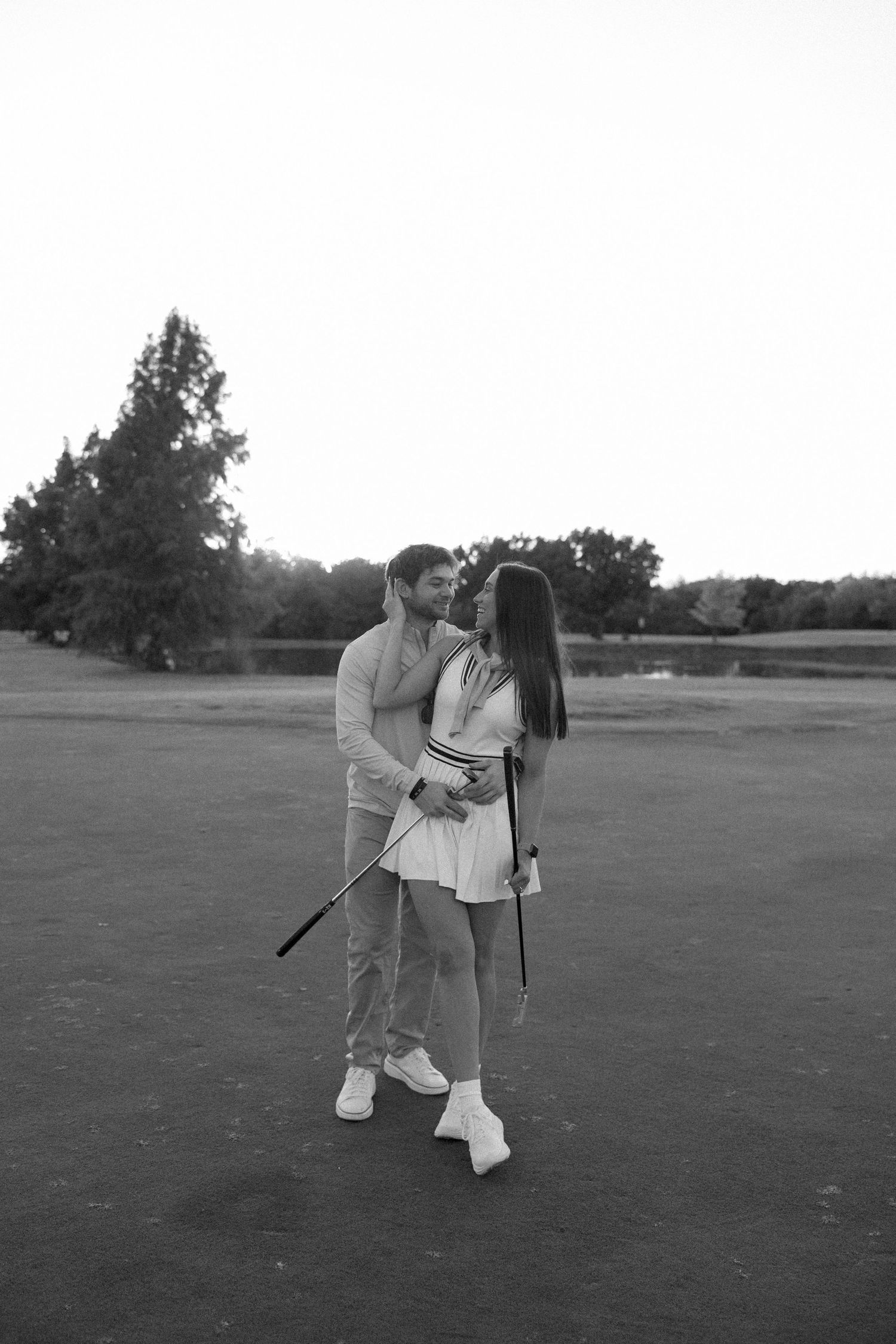 Romantic black and white photo of a couple sharing a moment on a golf course.