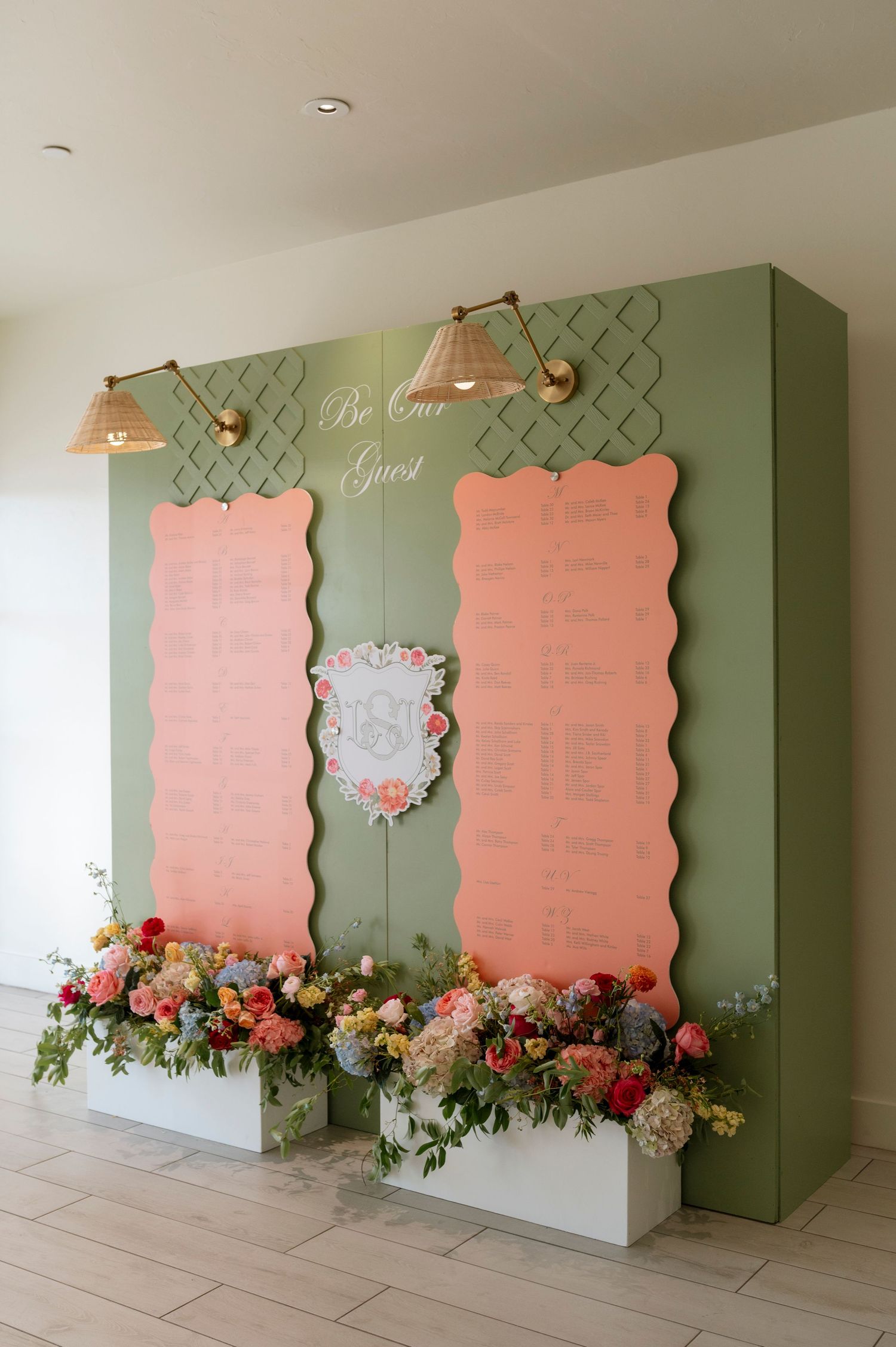 Wedding seating chart display with pink and sage green panels decorated with fresh flowers.