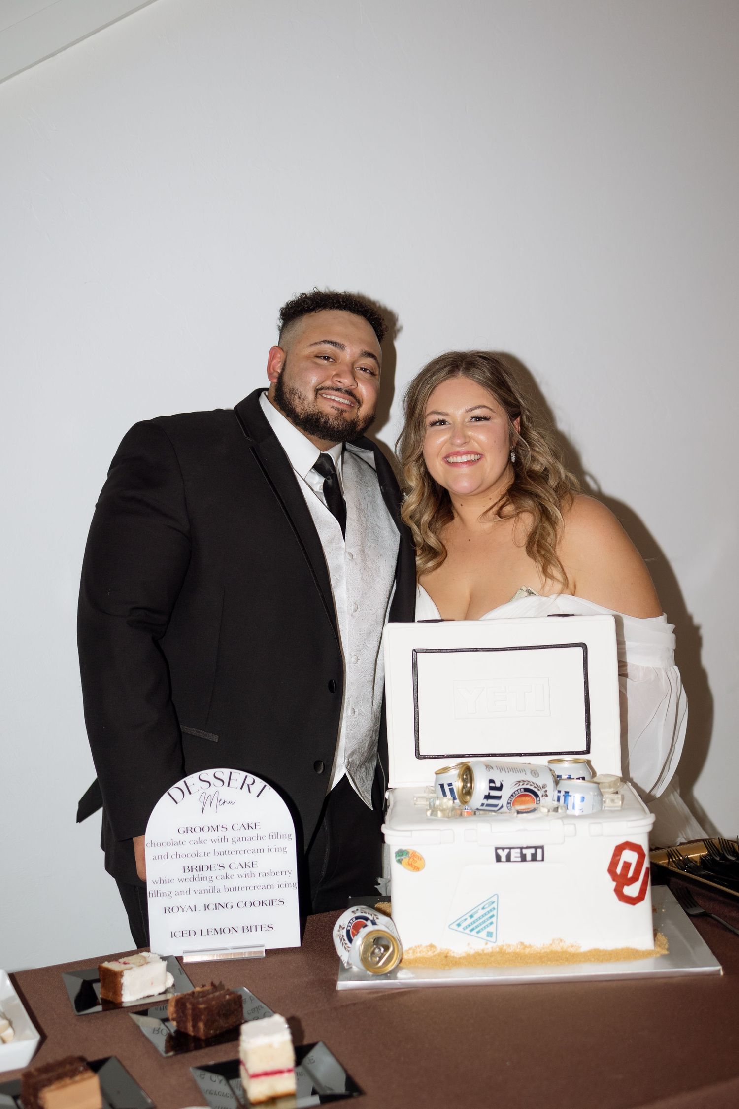 A couple poses with their decorated reception display featuring a YETI cooler and customized signage.